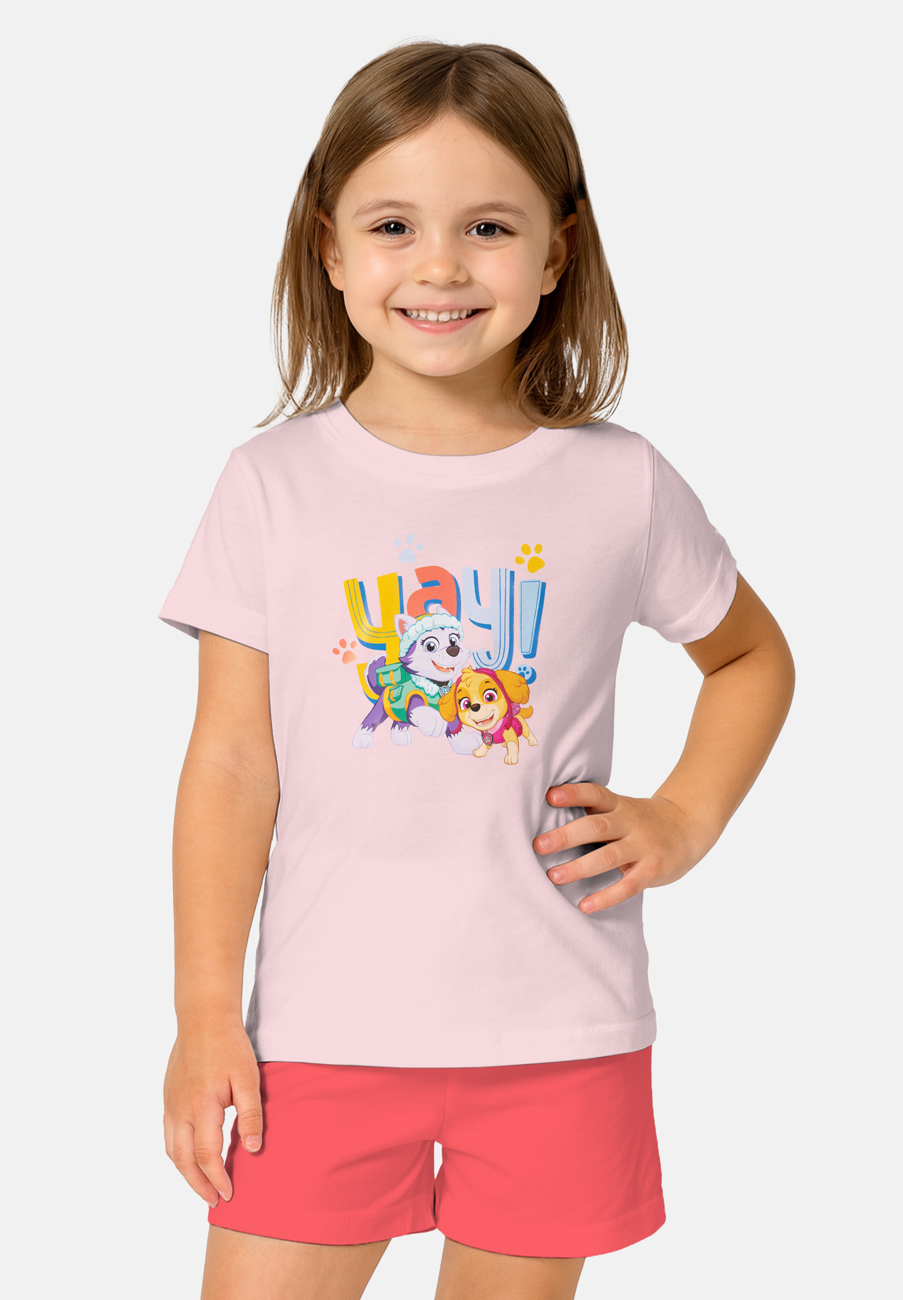 Ein Mädchen trägt ein hellrosa T-Shirt mit Paw Patrol-Motiv und roten Shorts.