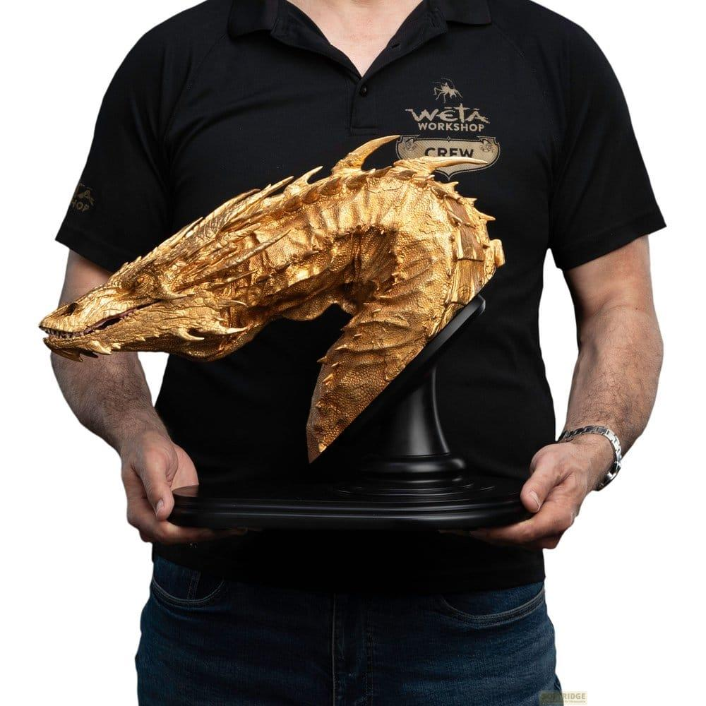 Goldene Drachenkopf-Statue auf schwarzem Sockel, gehalten von Person in schwarzem T-Shirt.