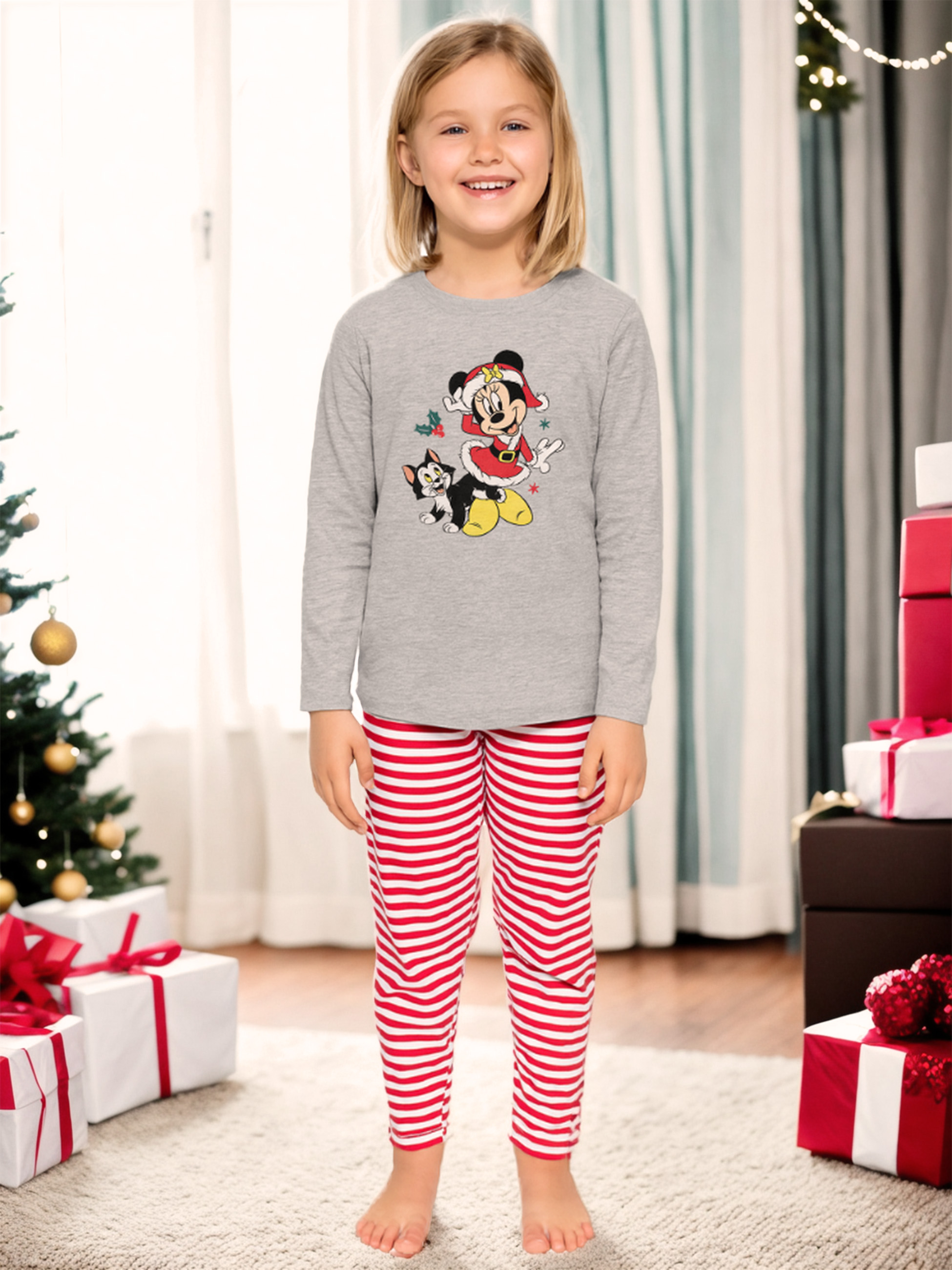 Ein Mädchen in gestreifter Pyjamahose und einem Mickey-Maus-Shirt steht vor Geschenken.