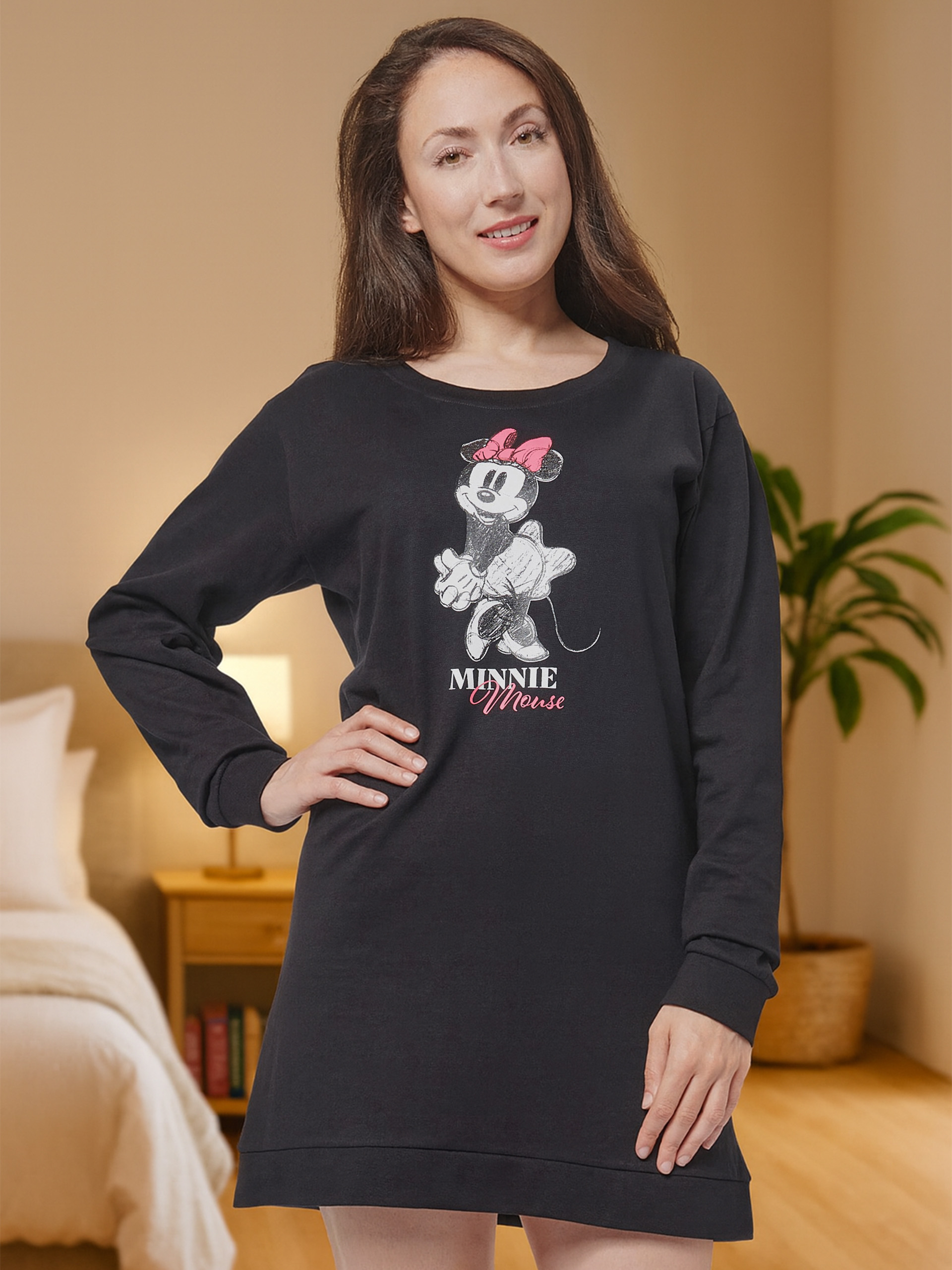 Frau in schwarzem Nachthemd mit Minnie Maus Aufdruck, steht in einem Schlafzimmer.