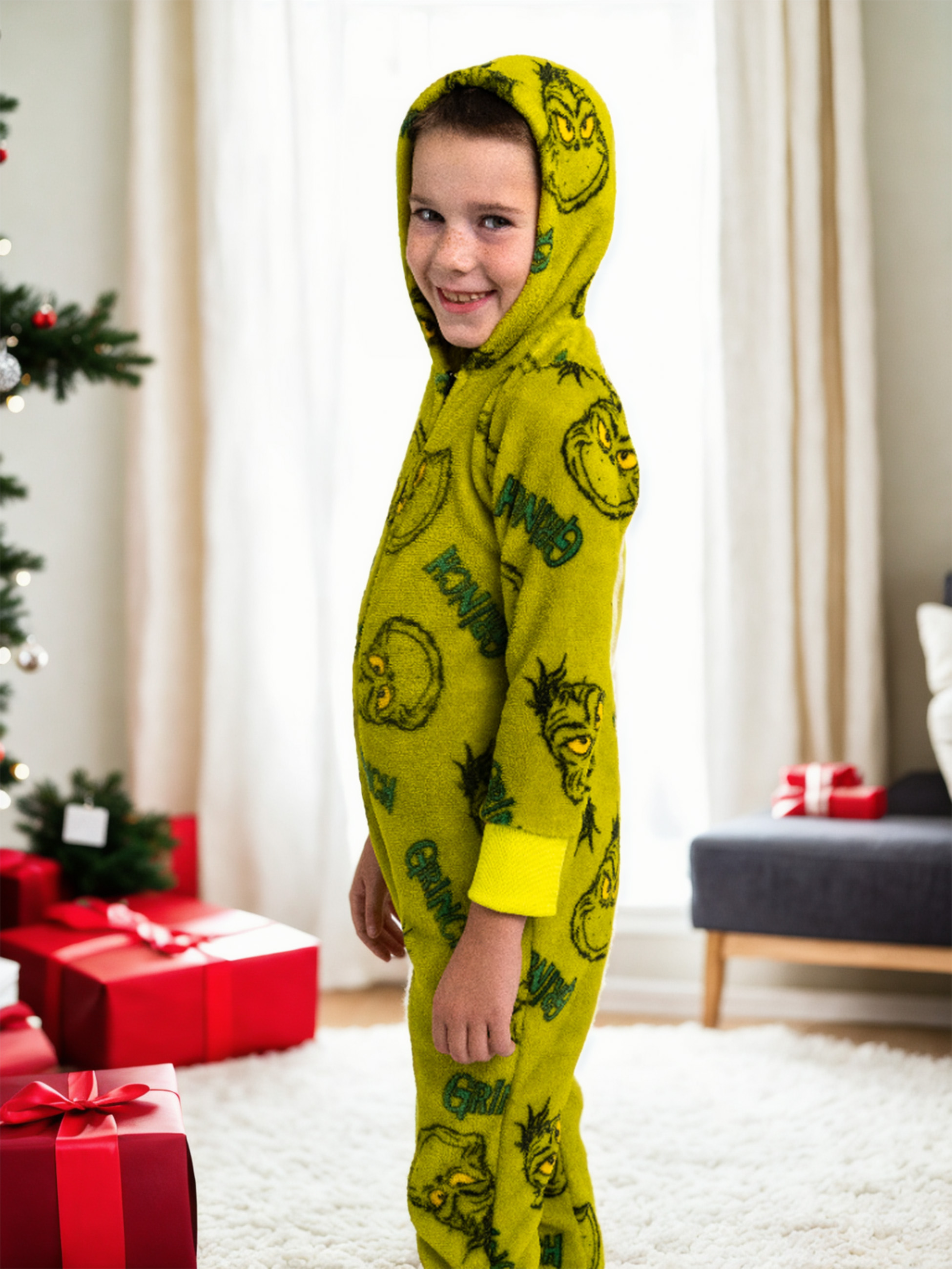Junge in grünem Grinch-Overall mit Kapuze, mit Weihnachtsgeschenken und Baum.