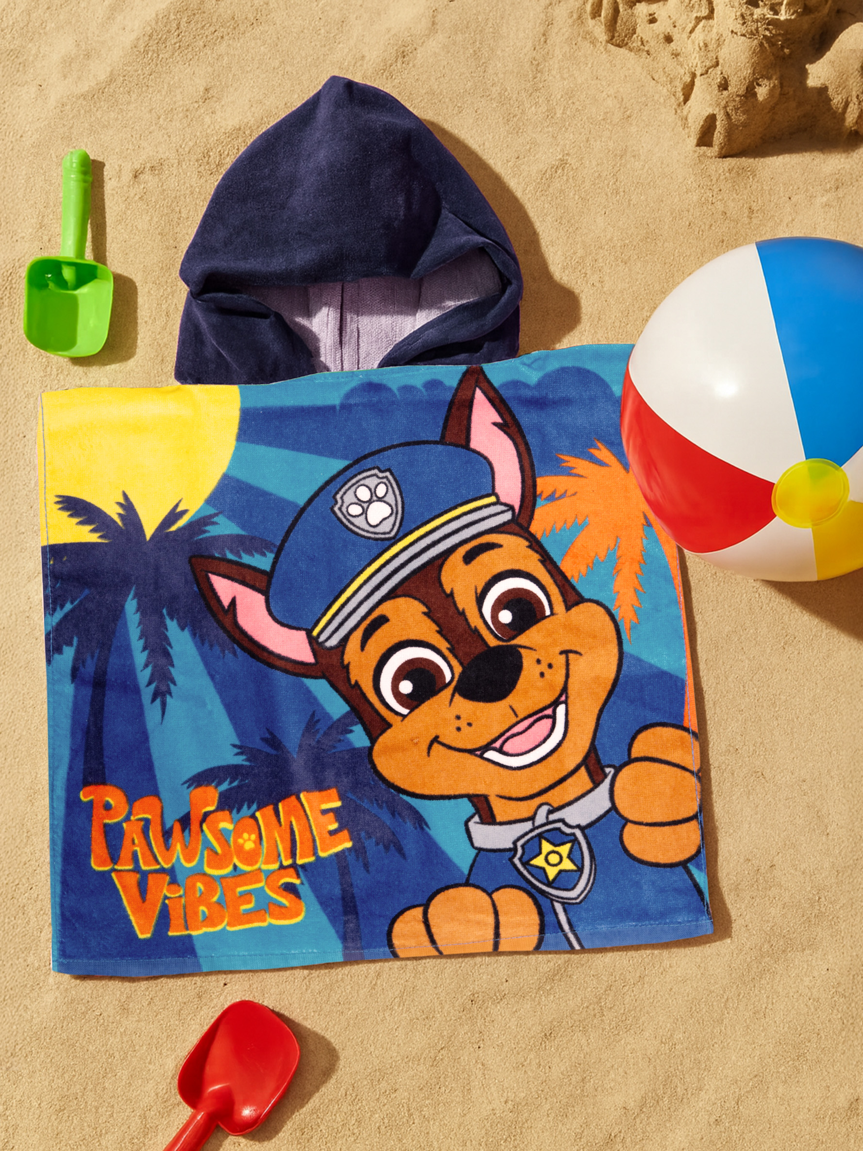 Ein Paw Patrol Handtuch mit Chase auf Sand, daneben Spielzeug und Ball.
