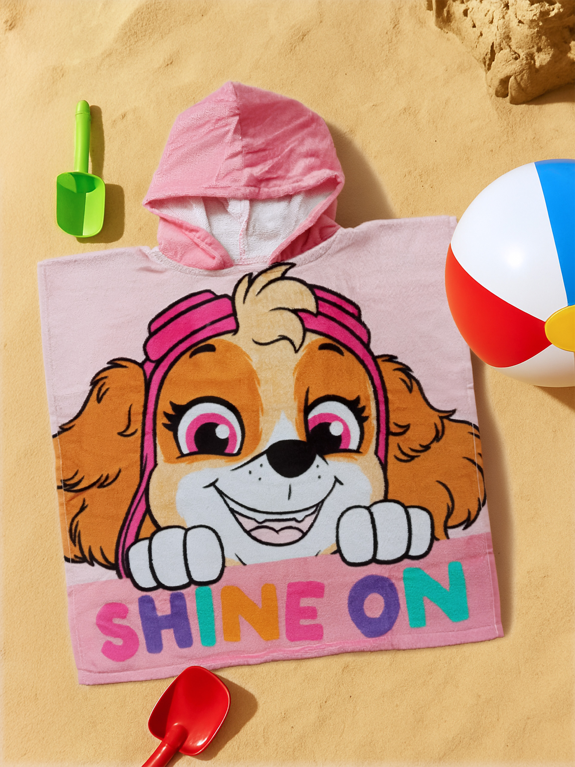 Ein rosa Kapuzenhandtuch mit Skye von Paw Patrol, Strandspielzeug und Ball auf Sand.