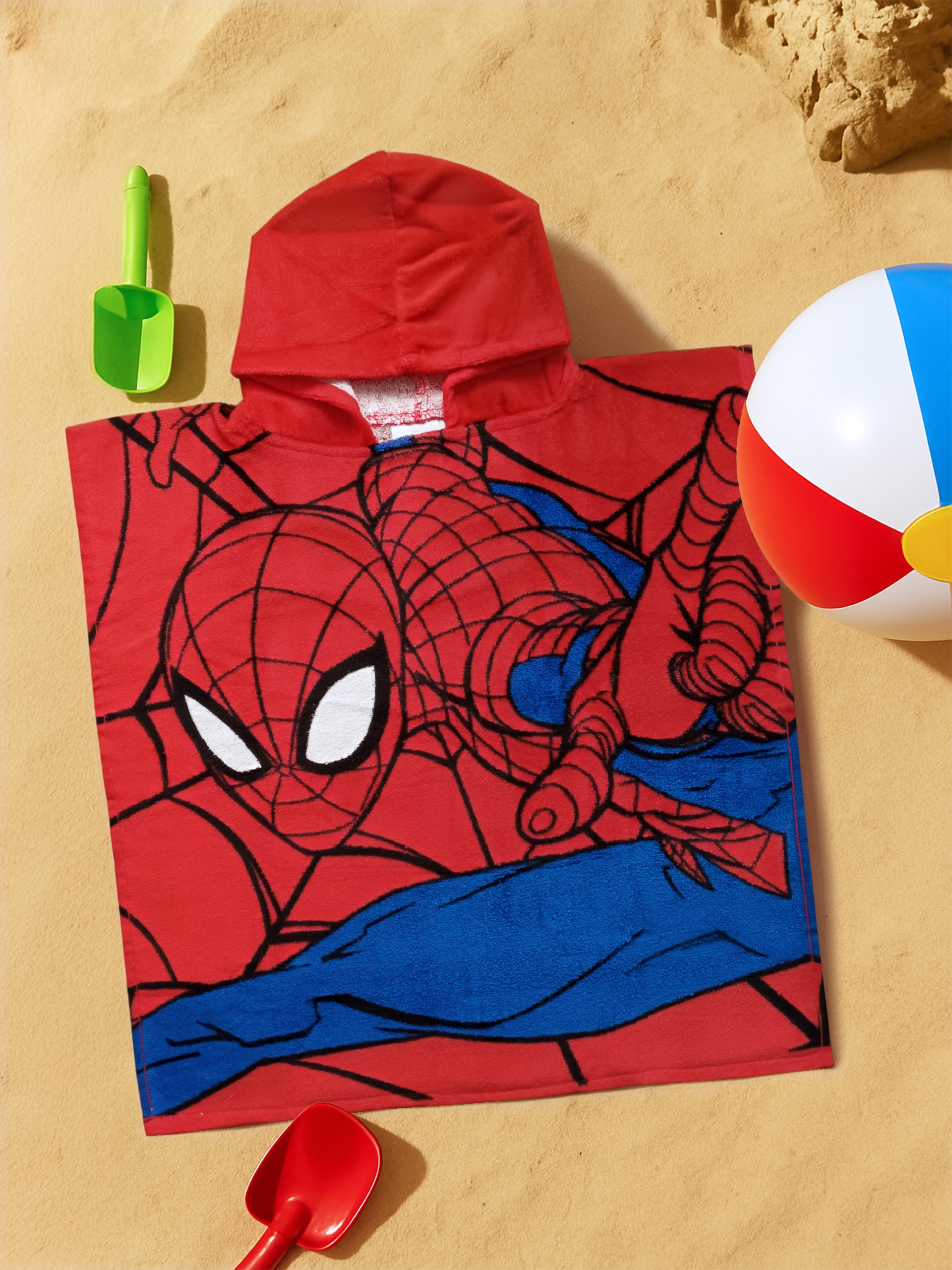 Ein rotes Kapuzenhandtuch mit Spiderman-Print liegt auf Sand, daneben Spielzeug.
