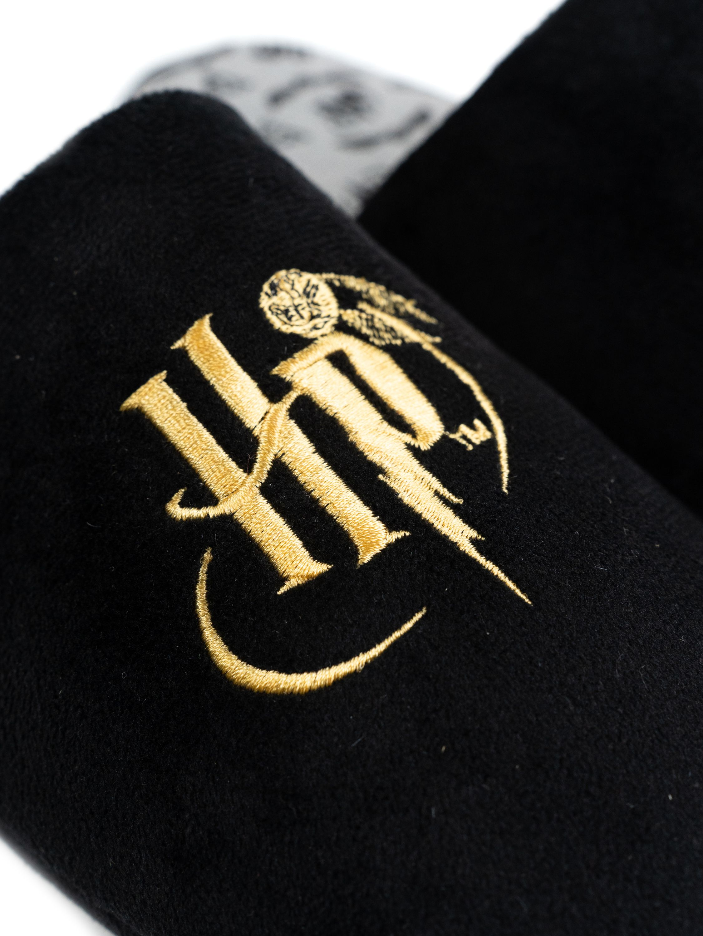 Schwarze Hausschuhe mit goldenem HP-Logo und Eulenmotiv auf weißem Hintergrund.