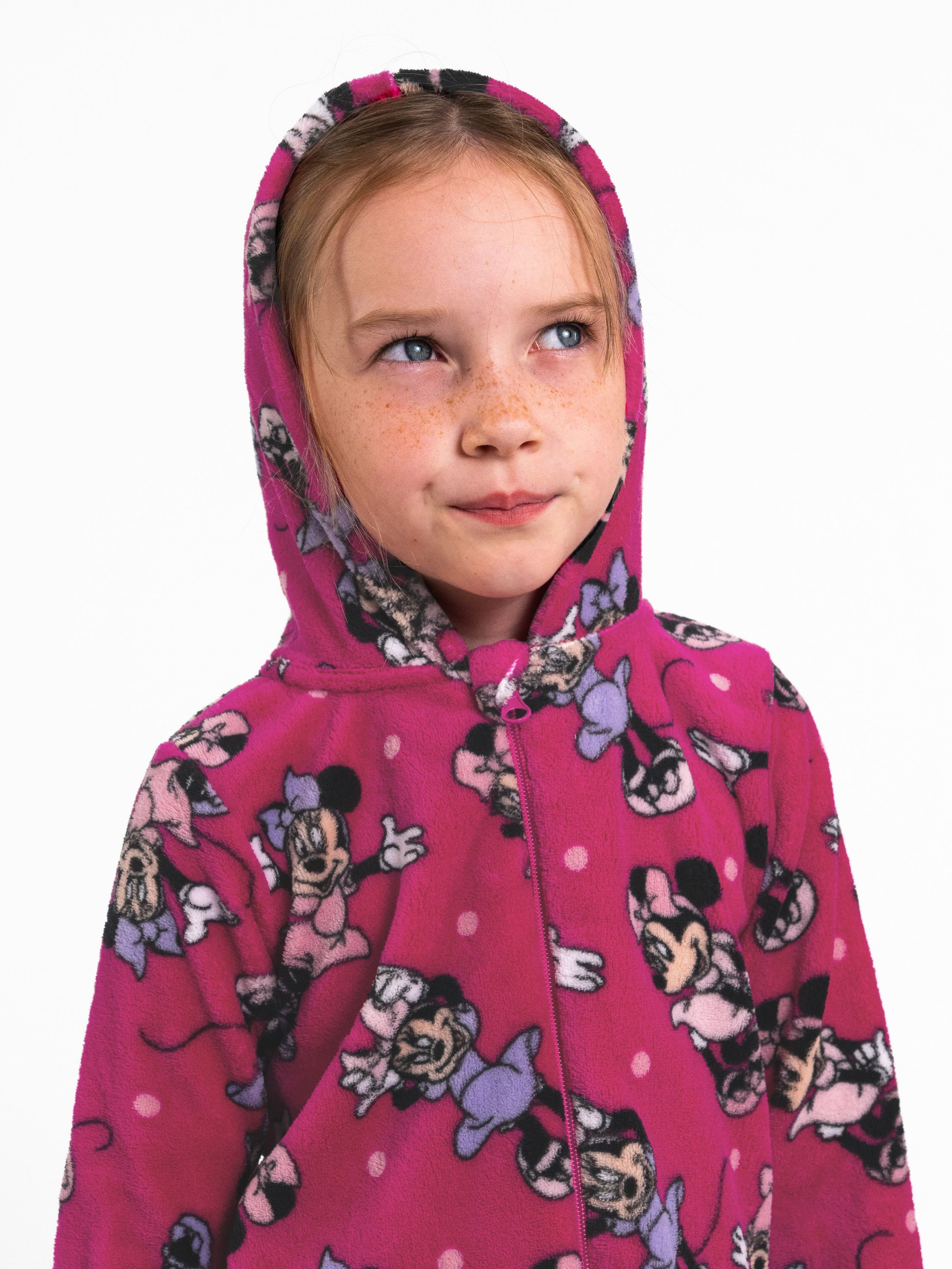 Ein junges Mädchen mit Sommersprossen trägt einen pinkfarbenen Schlafanzug mit Micky-Maus-Motiv.