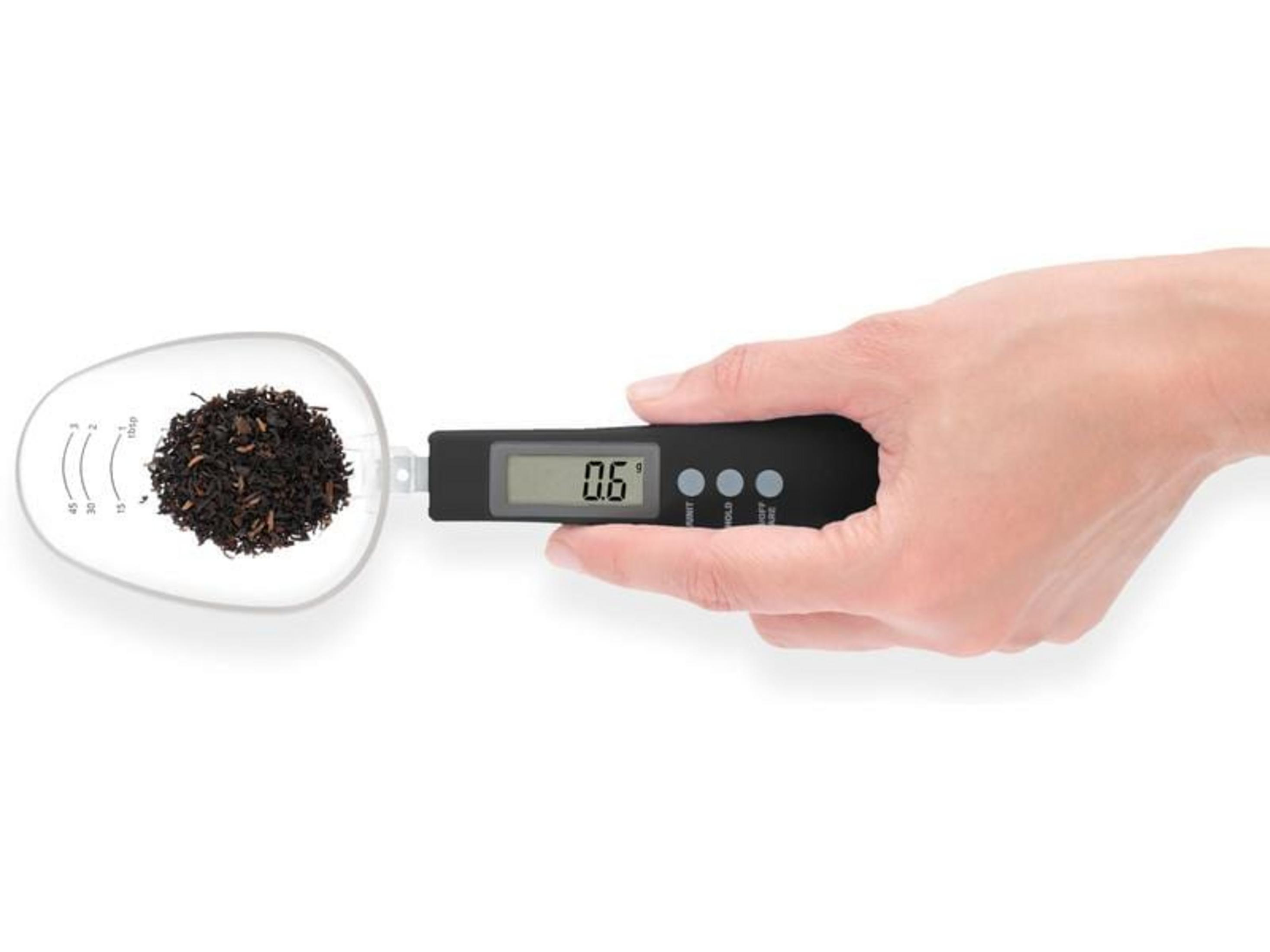 Une main tient une balance cuillère avec 0,6g de thé. La balance affiche 0,6g.