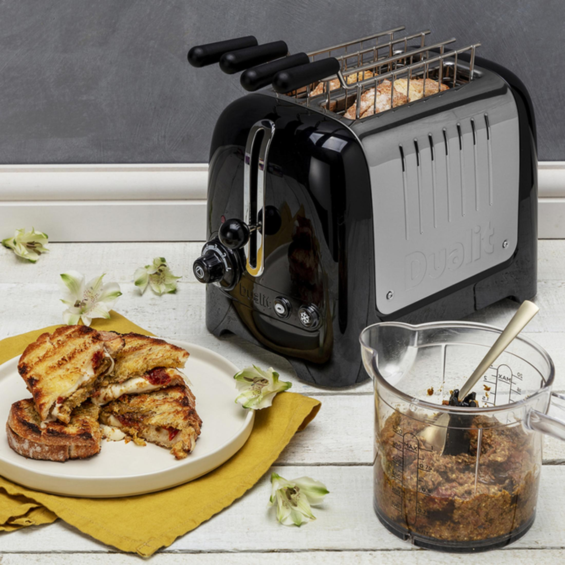 Ein schwarzer Toaster mit Toast, Sandwiches auf einem Teller und einem Messbecher voller Zutaten.