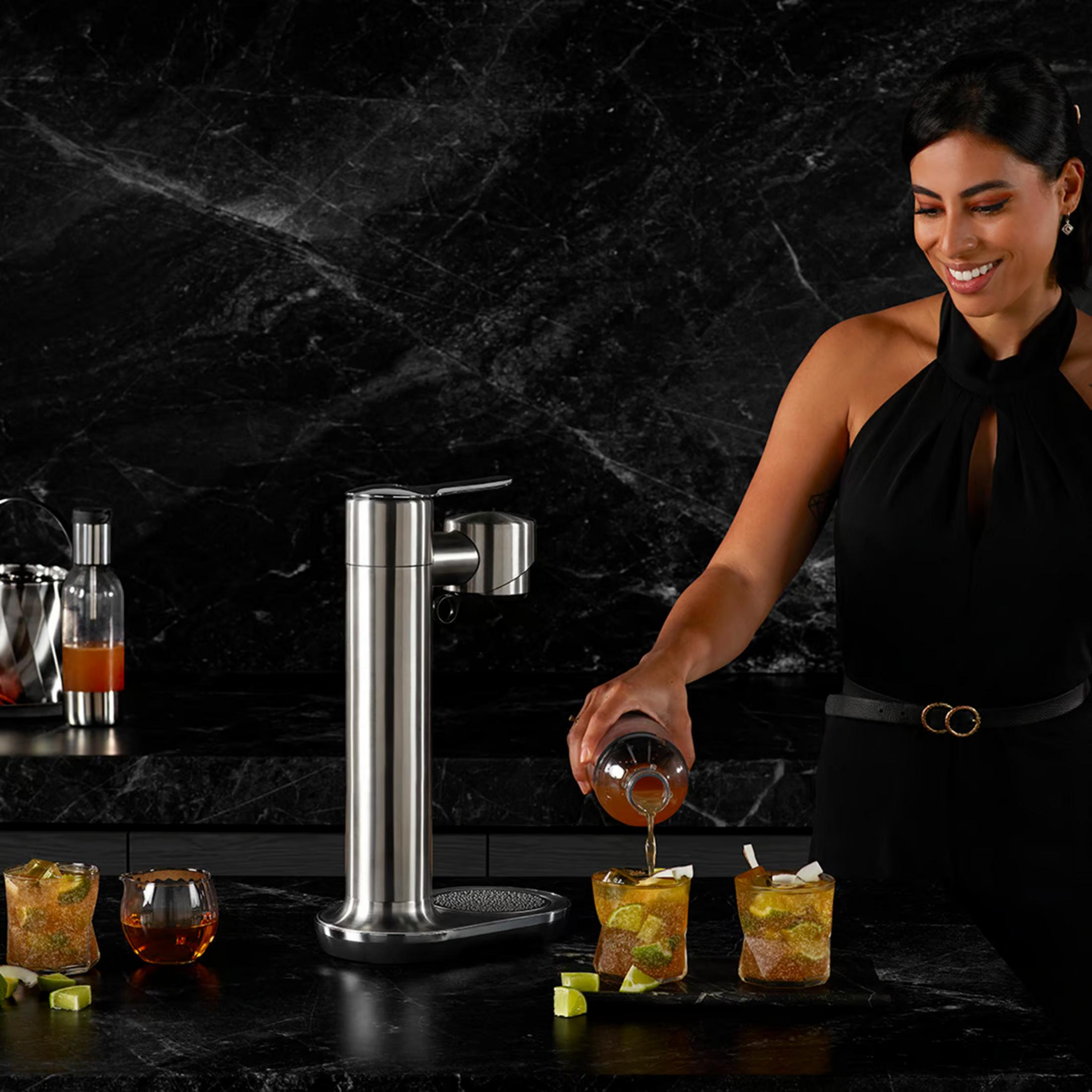 Eine Frau gießt Getränk in ein Glas mit Eis und Limette, neben einem Getränkespender.