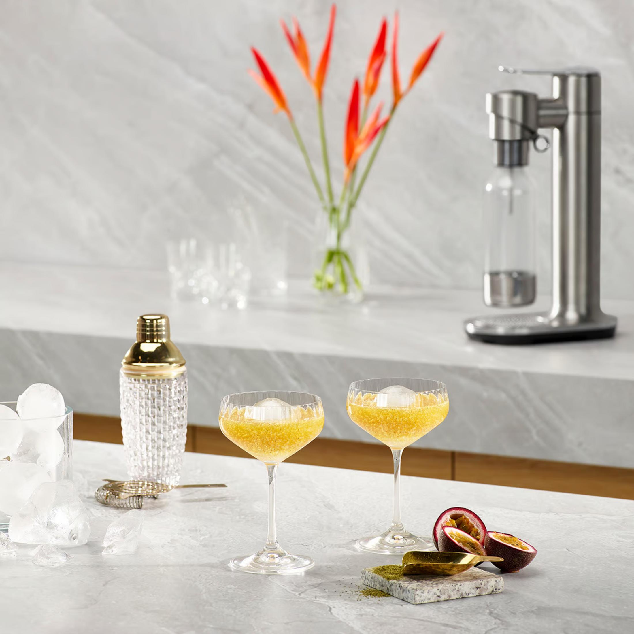 Zwei Cocktails mit Eis, ein Shaker, Passionsfrucht und ein Wassersprudler.