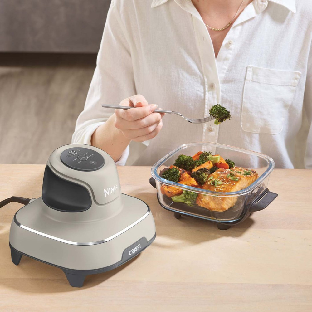 Un dispositivo Ninja Crispi accanto a un piatto di vetro con salmone e broccoli.