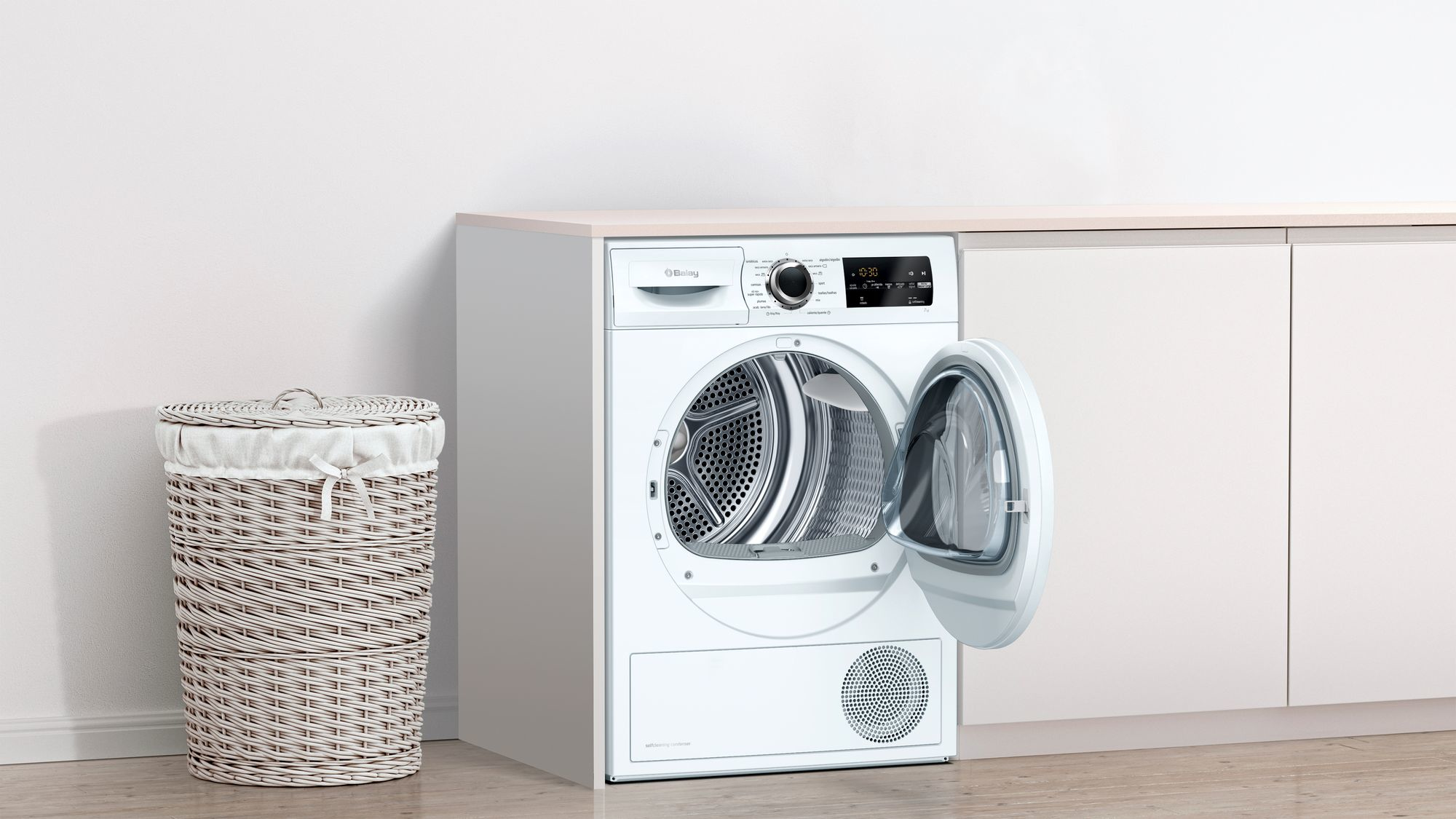 Una secadora blanca con la puerta abierta junto a una cesta de mimbre.