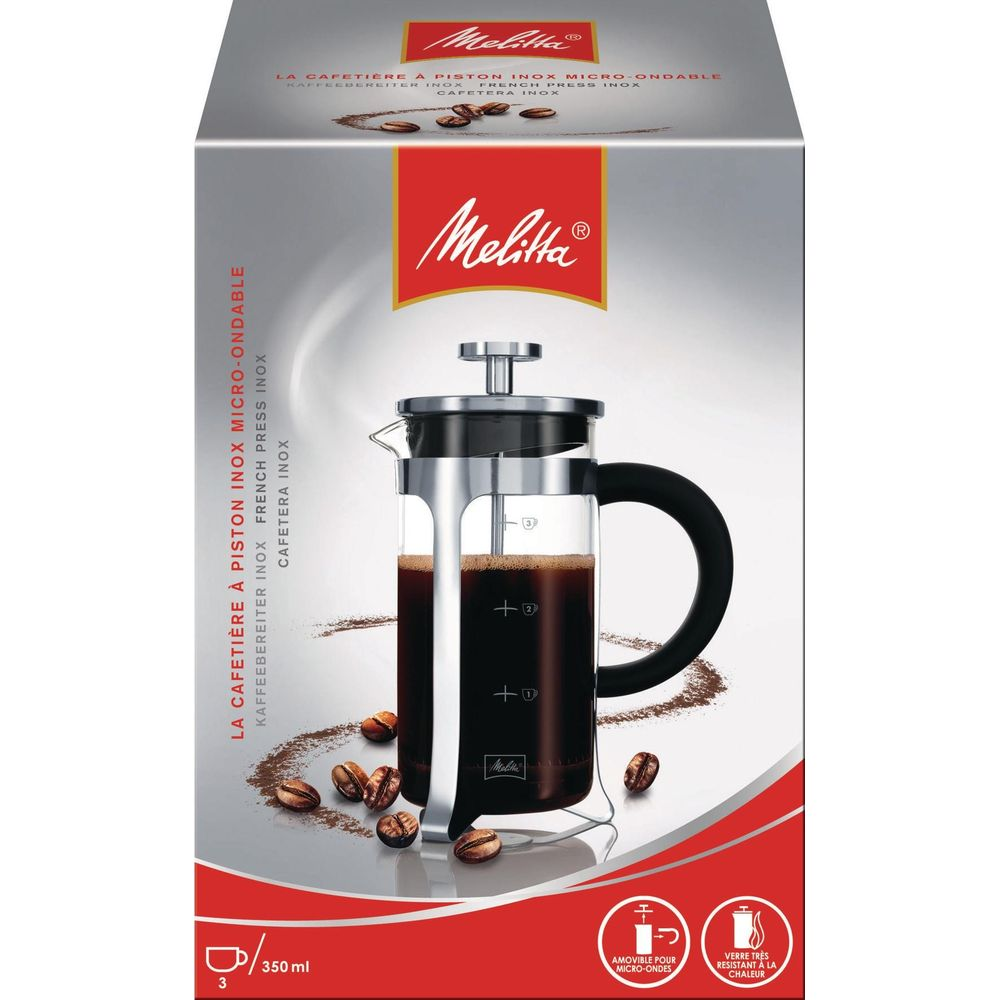 Una cafetera de prensa de vidrio con mango negro, llena de café, junto a granos de café.