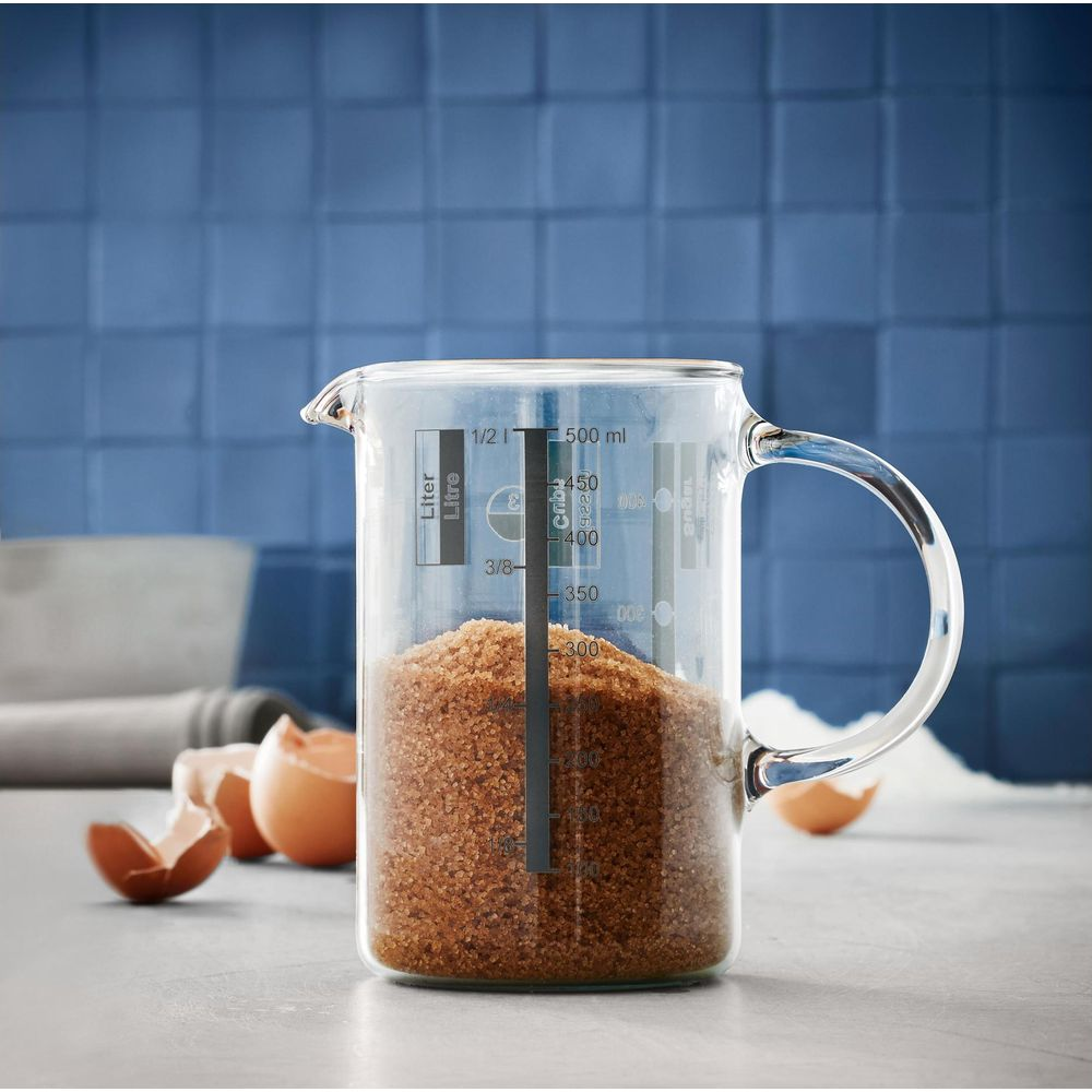 Messbecher mit braunem Zucker, Eierschalen und Mehl auf einer Arbeitsplatte.