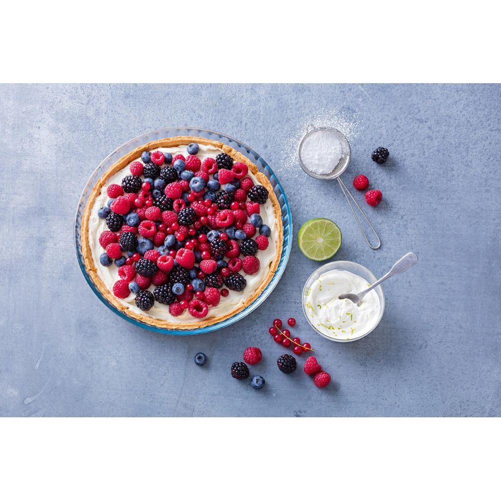 Beeren-Tarte mit Sahne, Limette und Puderzucker auf blauem Hintergrund.