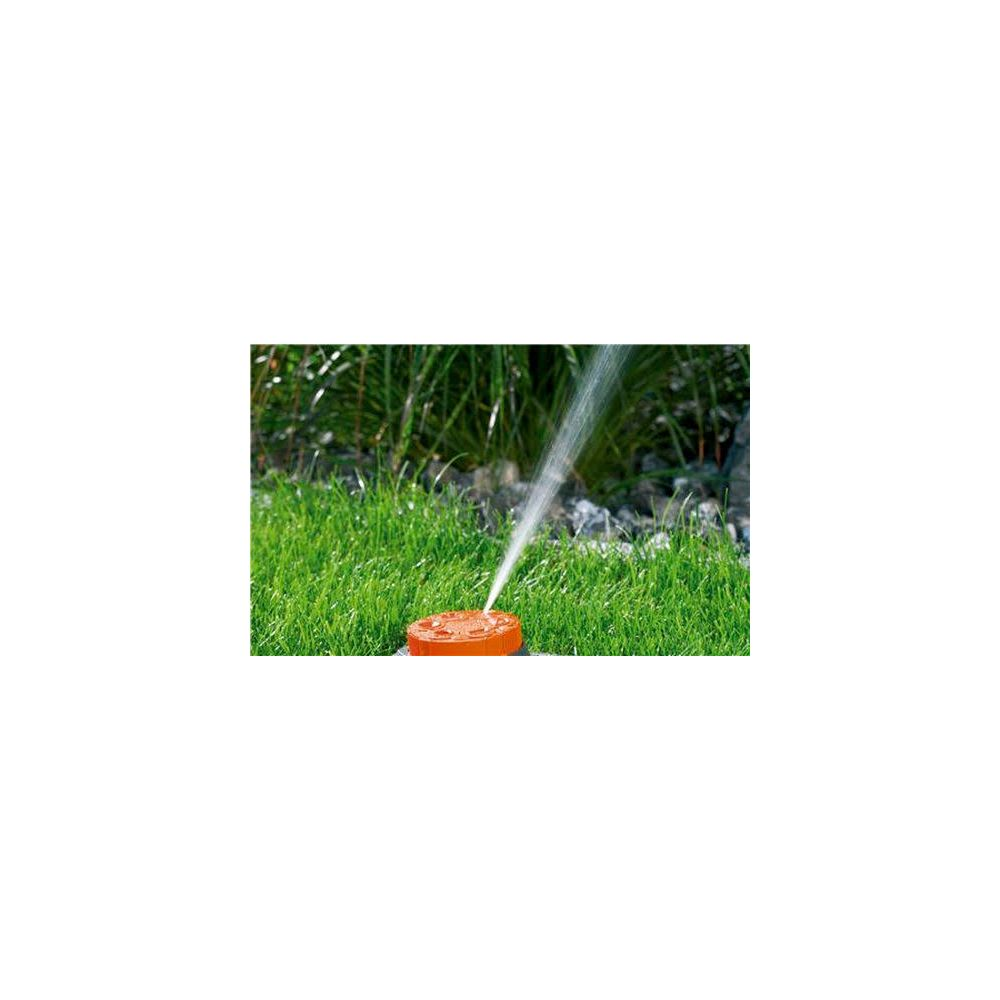 Ein oranger Sprinkler bewässert grünes Gras, mit Steinen und Pflanzen im Hintergrund.