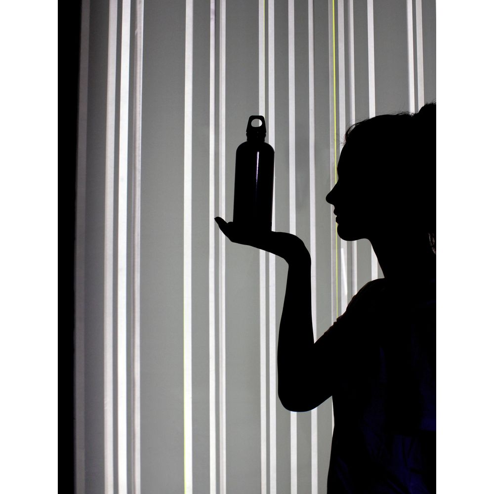 Silhouette einer Frau, die eine Flasche vor einem Hintergrund aus vertikalen Streifen hält.