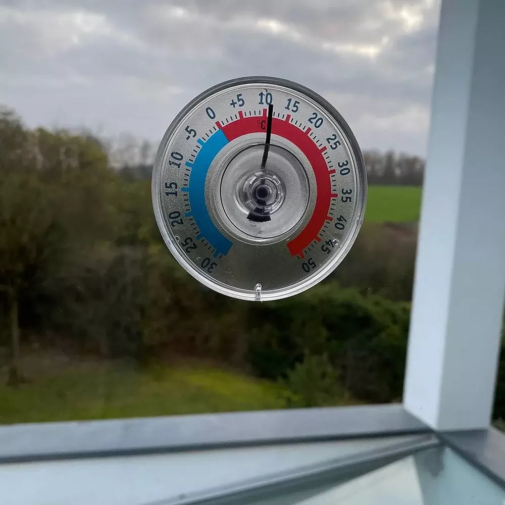 Ein Thermometer zeigt 10 Grad Celsius an, mit Blick auf eine grüne Landschaft.