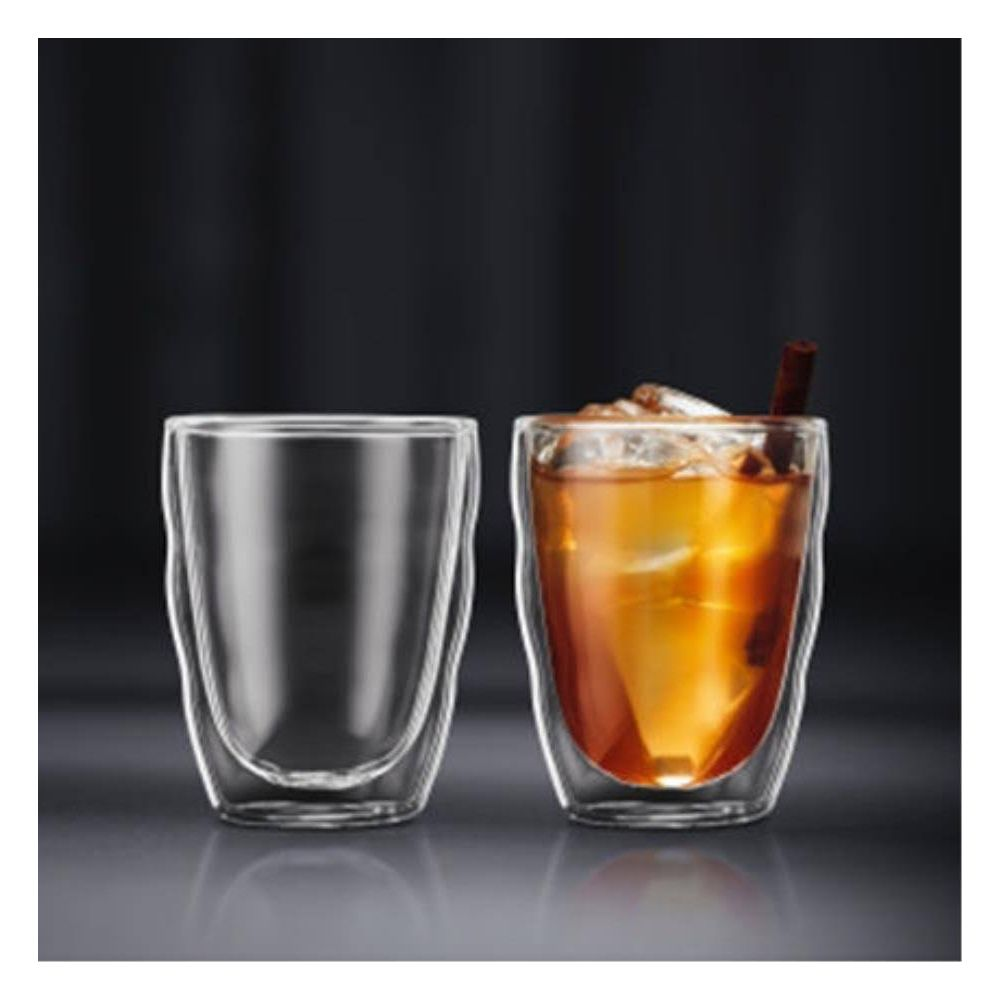 Ein leeres Glas neben einem Glas mit Eis und Zimtstange.