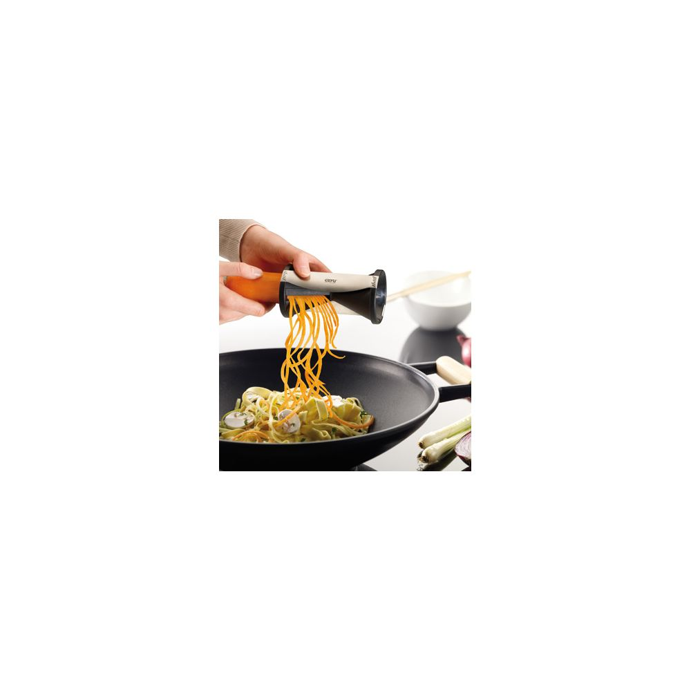 Eine Hand benutzt einen Spiralschneider, um Karottenstreifen in einen Wok zu schneiden.