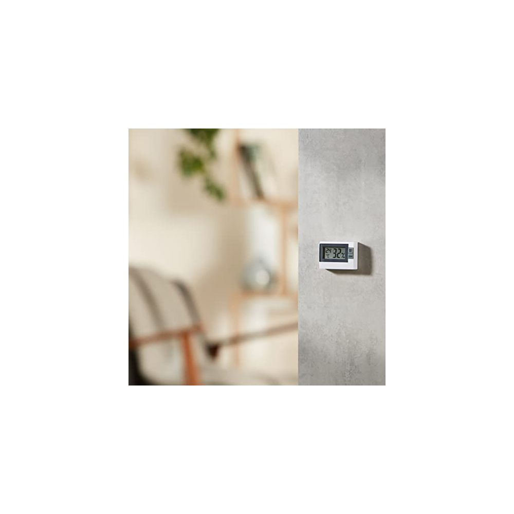 Ein digitales Thermometer mit 32,2 Grad auf einer Wand im Hintergrund eines Wohnzimmers.