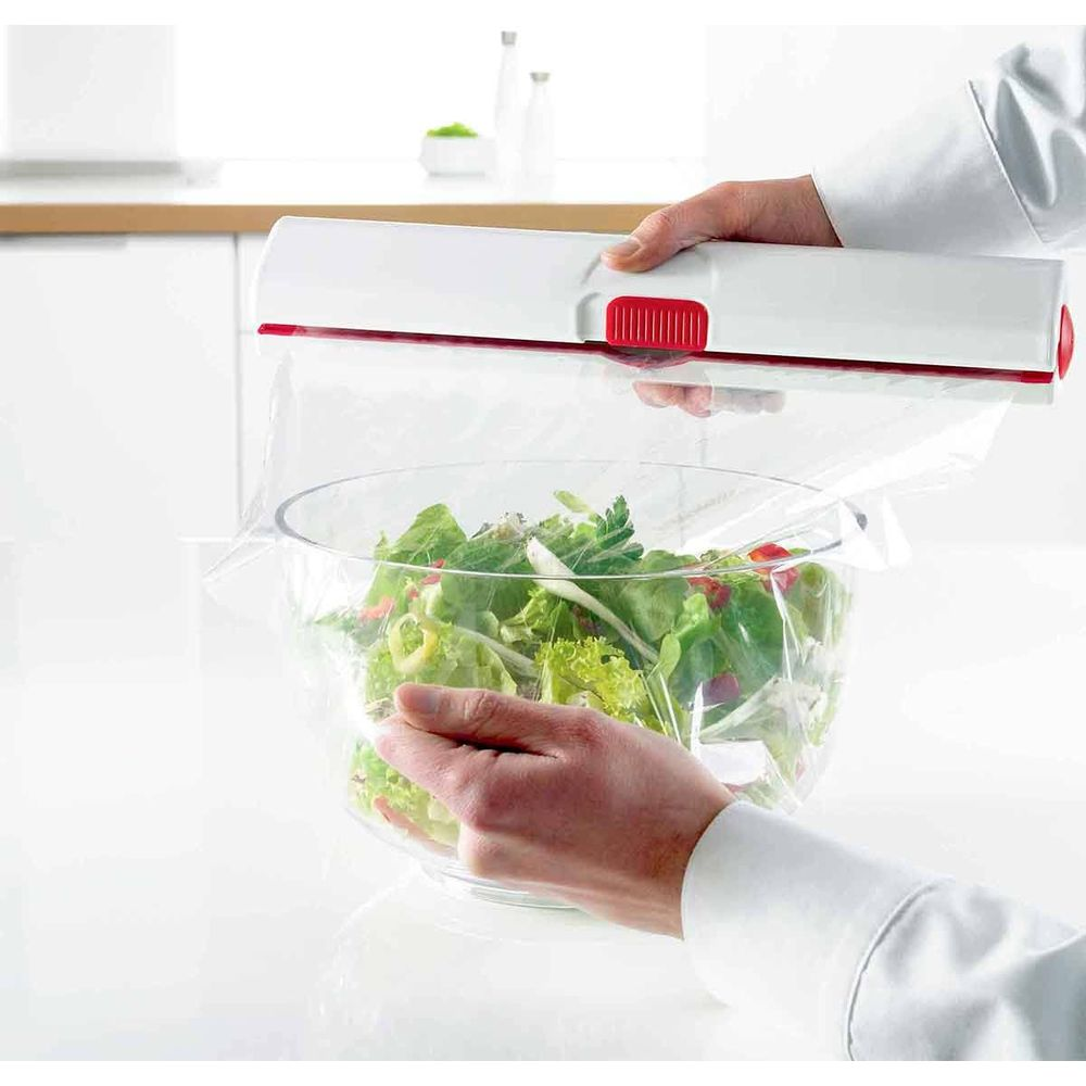 Hände verpacken einen Salat in einer Schüssel mit Frischhaltefolie.