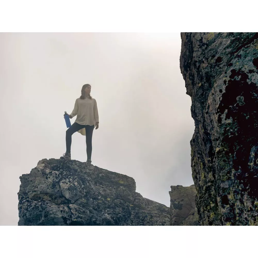 Eine Frau steht auf einem Felsen mit einer blauen Wasserflasche.