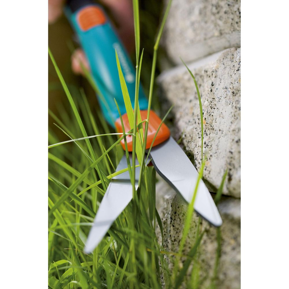 Gartenschere schneidet Gras neben Steinmauer. Nahaufnahme.