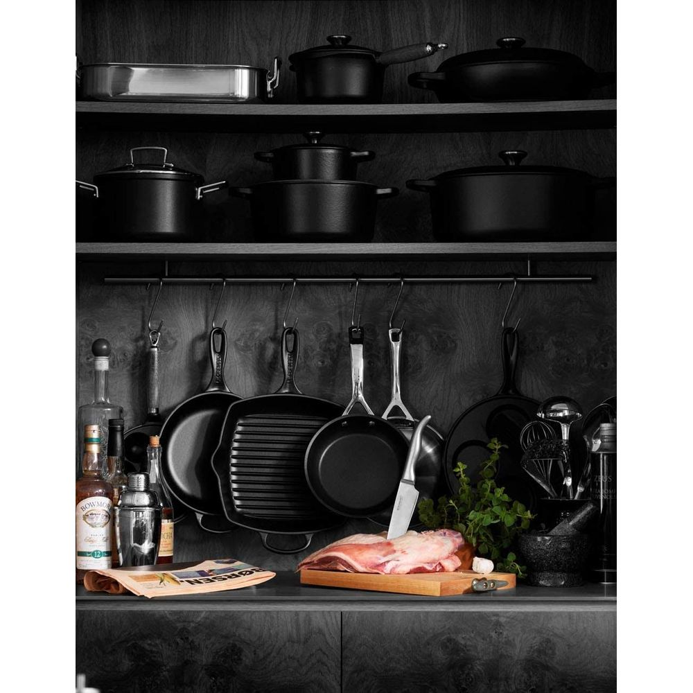 Ustensiles de cuisine : casseroles, poêles, couteau, viande sur planche, herbes.
