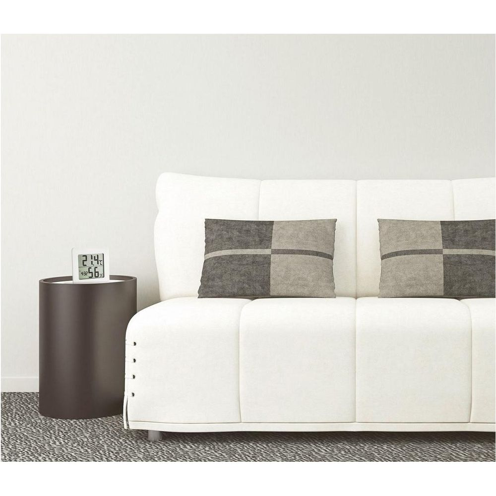 Ein weißes Sofa mit zwei Kissen steht neben einem dunklen Beistelltisch mit Digitaluhr.