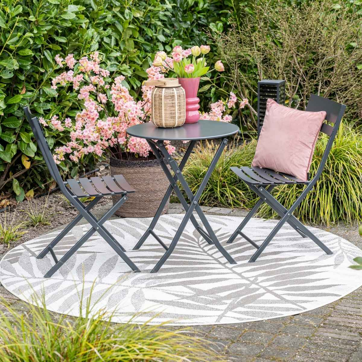 Een ronde tuintafel met twee stoelen op een vloerkleed met bladmotief.