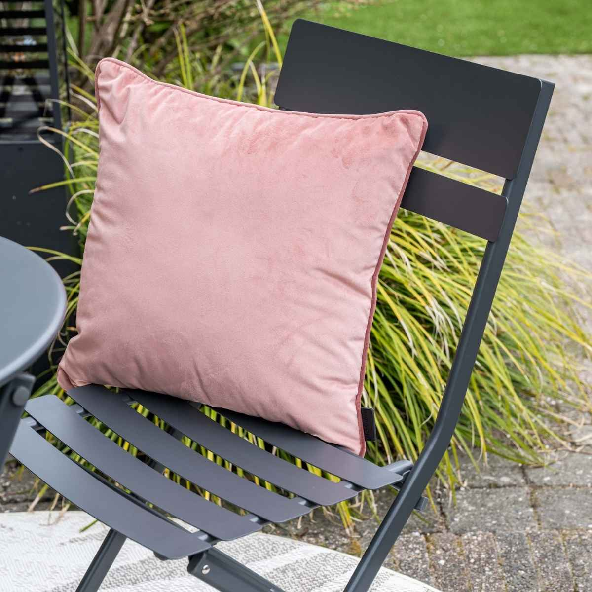 Een roze kussen op een donkergrijze buitenstoel.