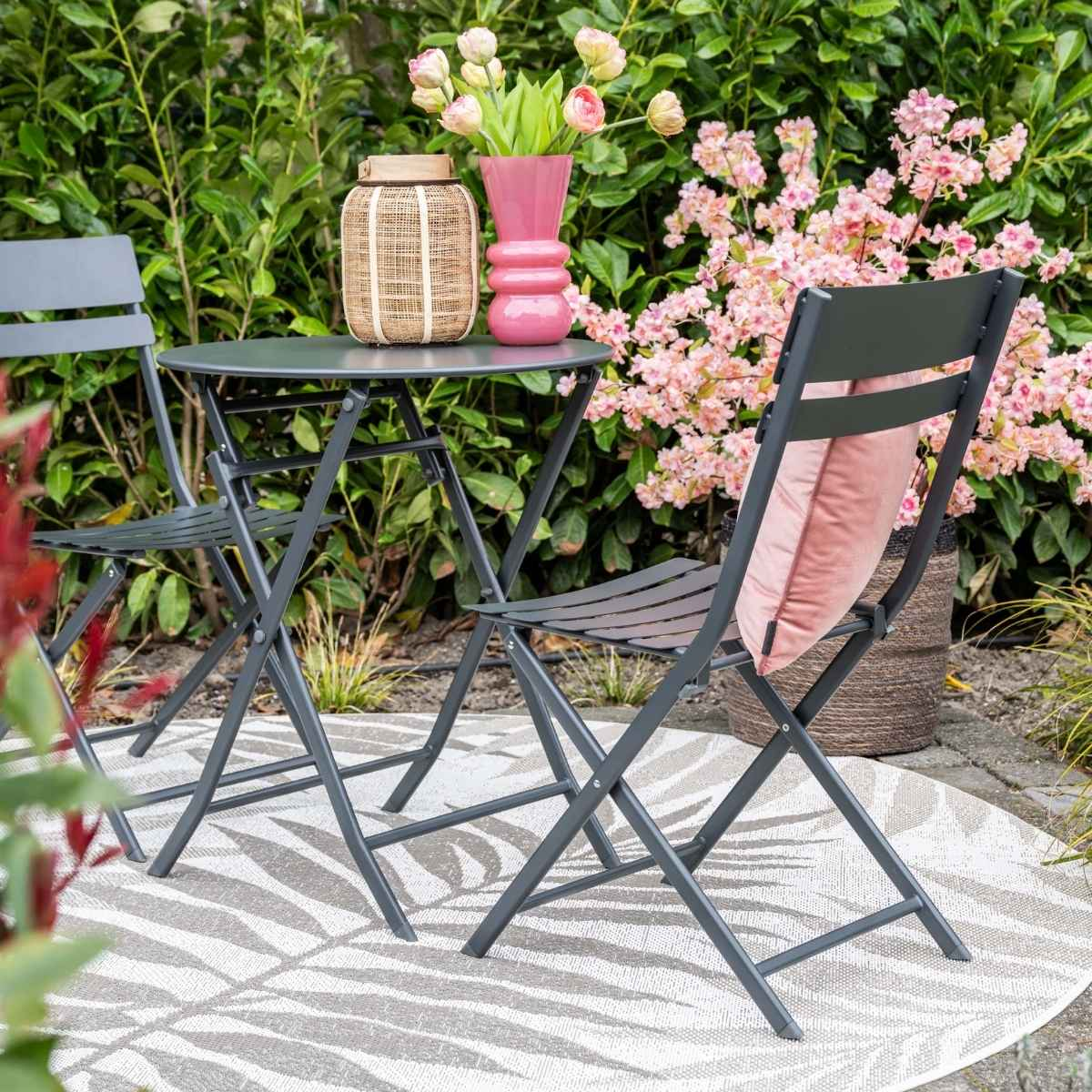 Grijs tuinmeubilair met kussens en bloemen op een ronde mat.