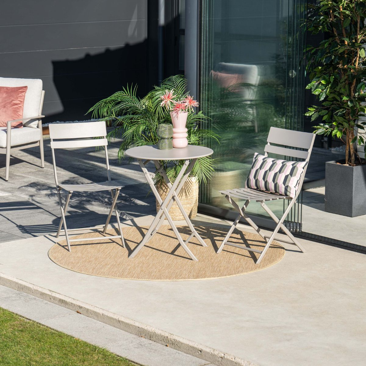 Een ronde mat met een grijze klaptafel en twee stoelen op een terras.
