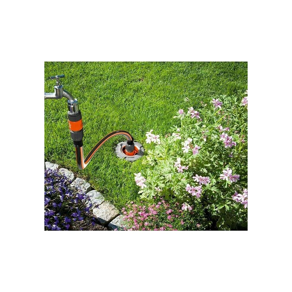 Gartenschlauchanschluss an Wasserhahn und Rasen mit Blumen.