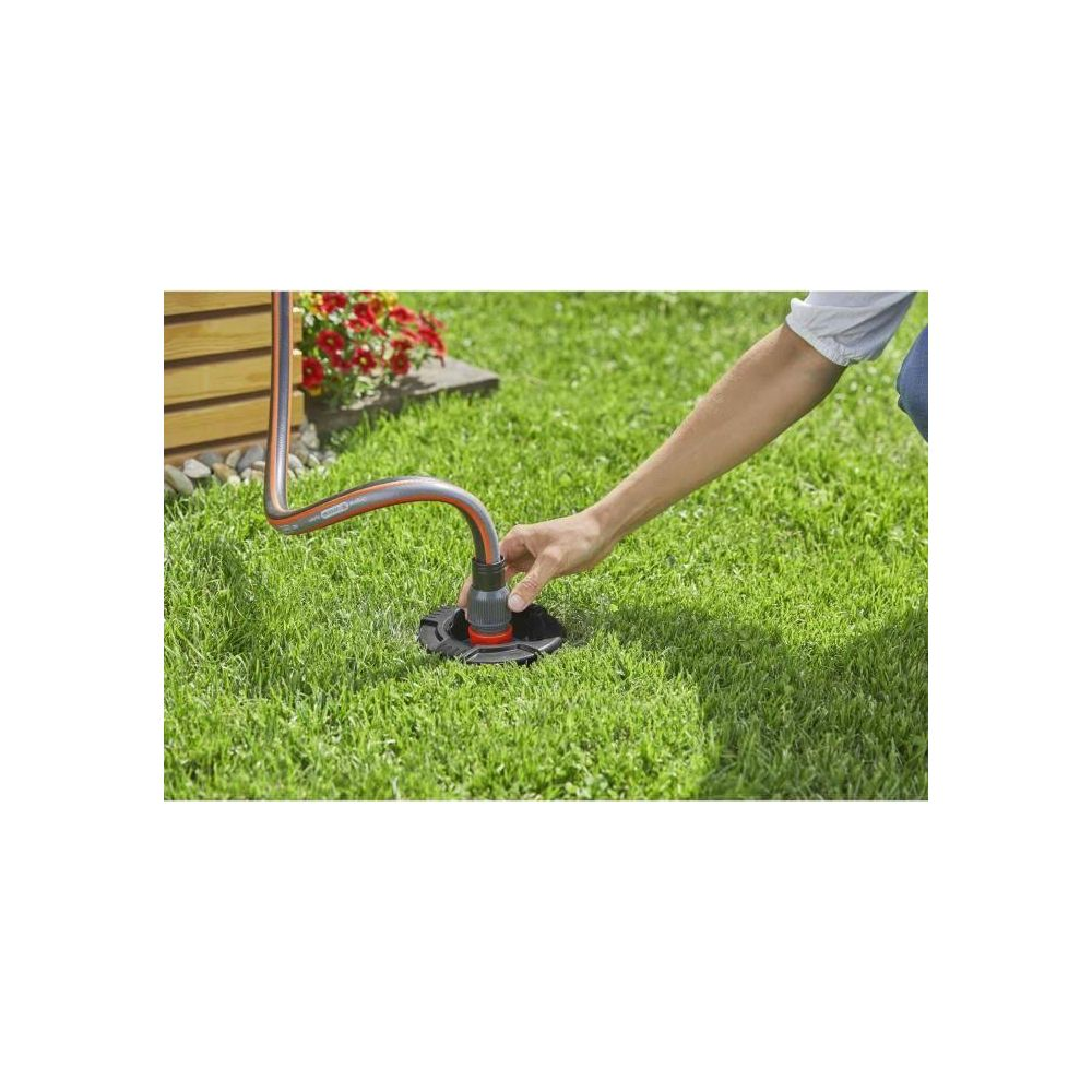 Hand steckt Gartenschlauch in Bodenregner. Rot-grauer Schlauch, schwarzer Regner.