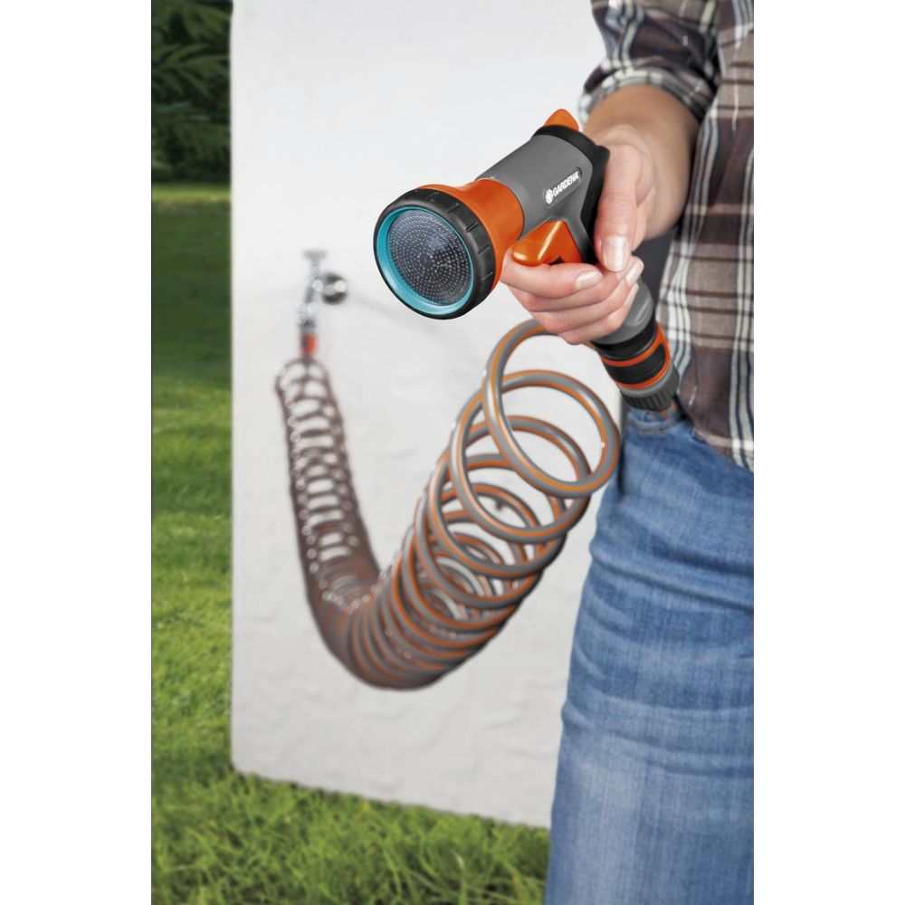 Person hält Gartenschlauch mit Sprühkopf, der an einer Wand befestigt ist.