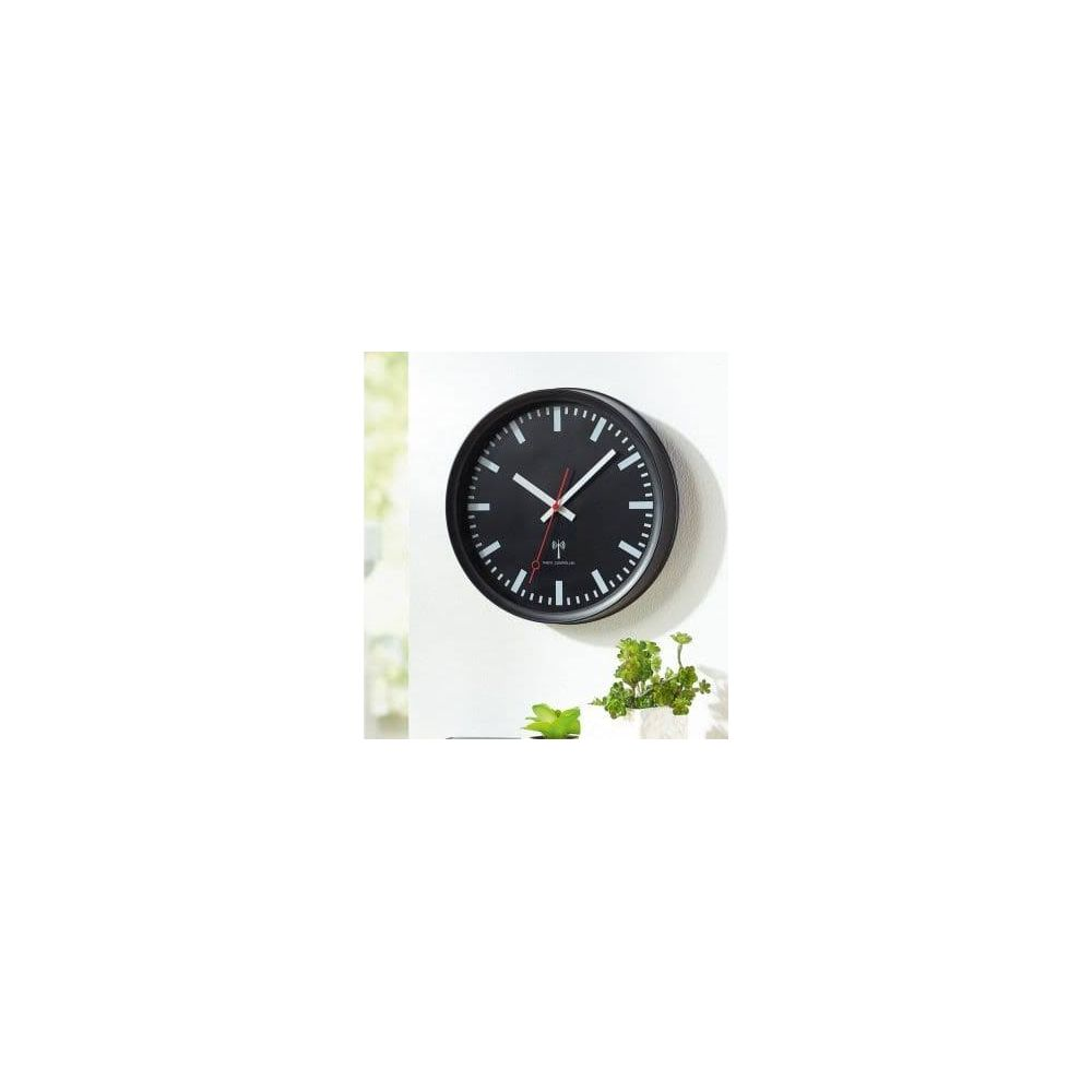Eine schwarze Wanduhr mit weißen Markierungen und roten Zeigern hängt an einer weißen Wand.
