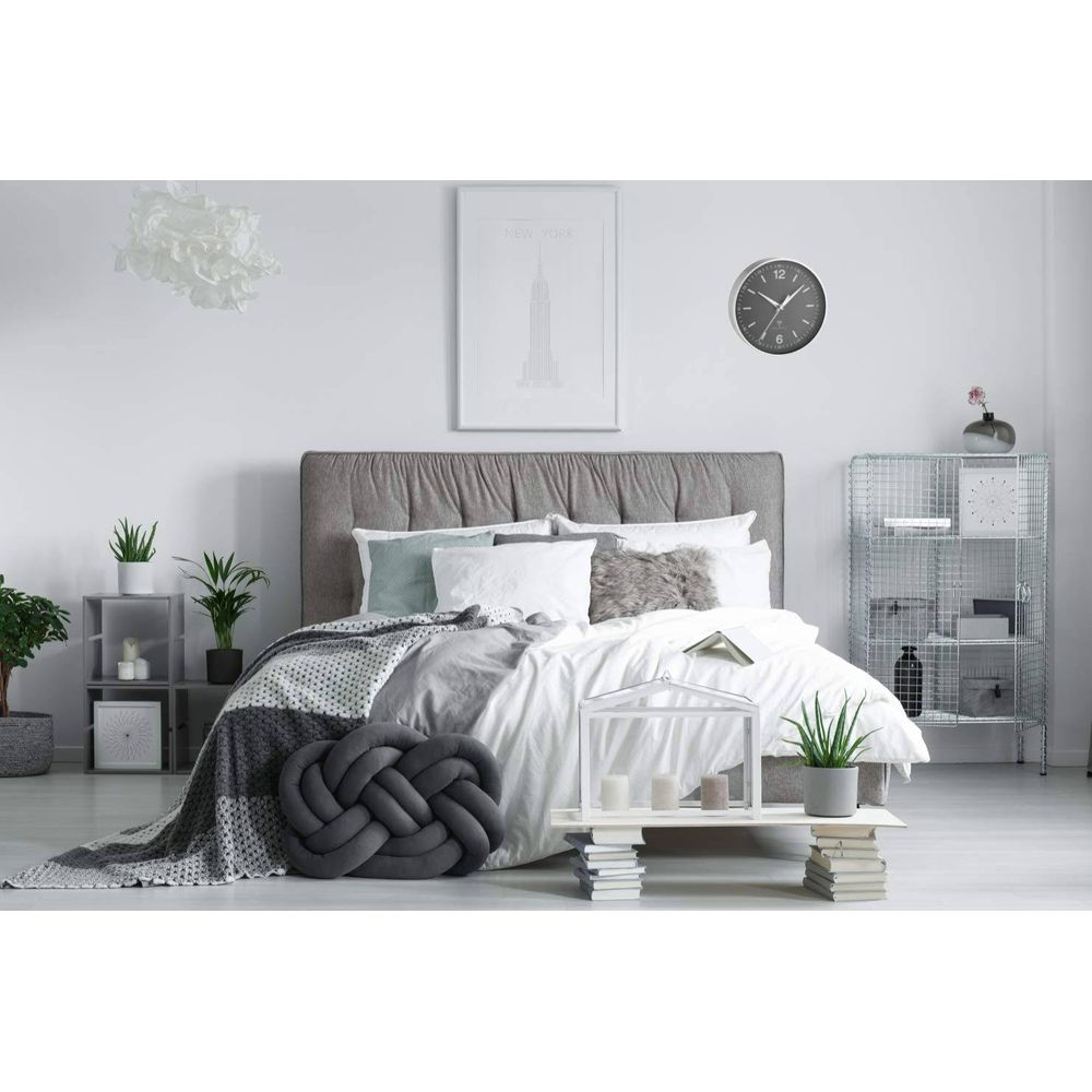 Modernes Schlafzimmer mit grauem Bett, weißen Kissen und einem geflochtenen Kissen.