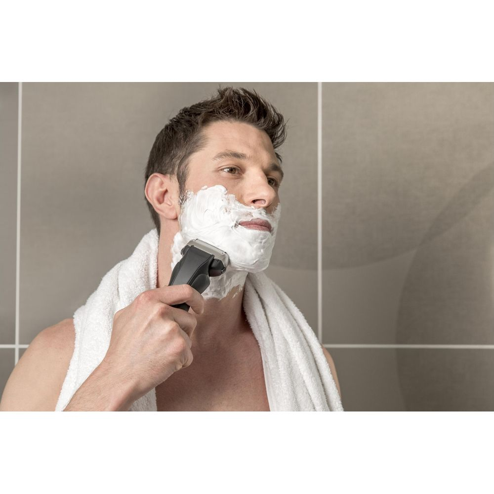Mężczyzna z pianką do golenia na twarzy używa golarki elektrycznej.