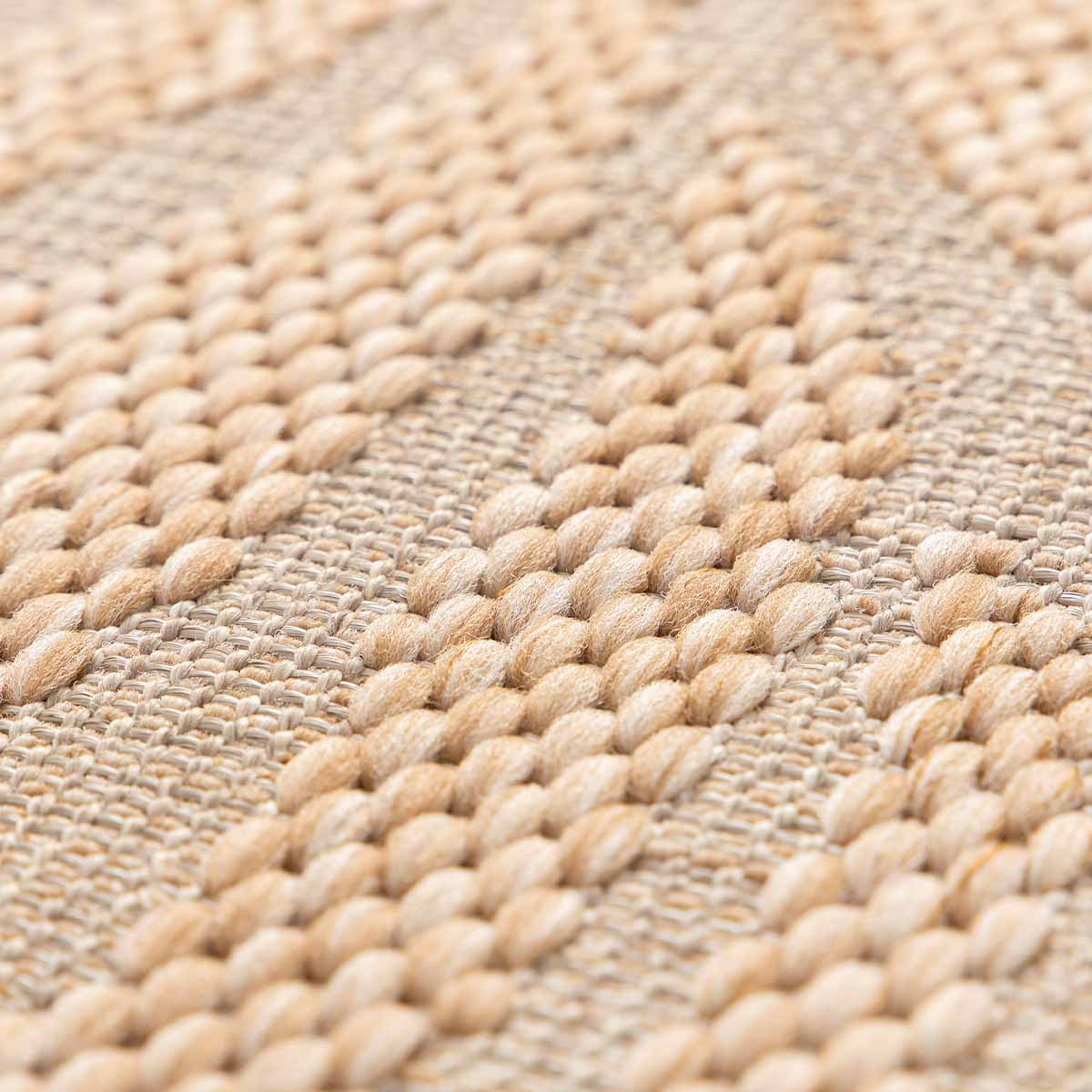 Close-up van een beige vloerkleed met geometrisch patroon van dikke draden.