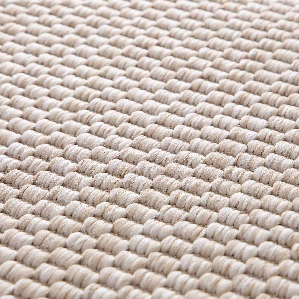 Close-up van een beige tapijt met een zichtbare geweven textuur.