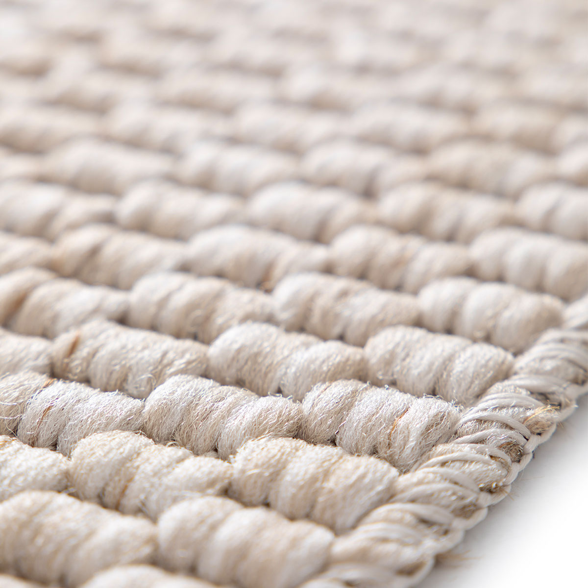 Close-up van een beige vloerkleed met geweven patroon van gedraaide koorden.