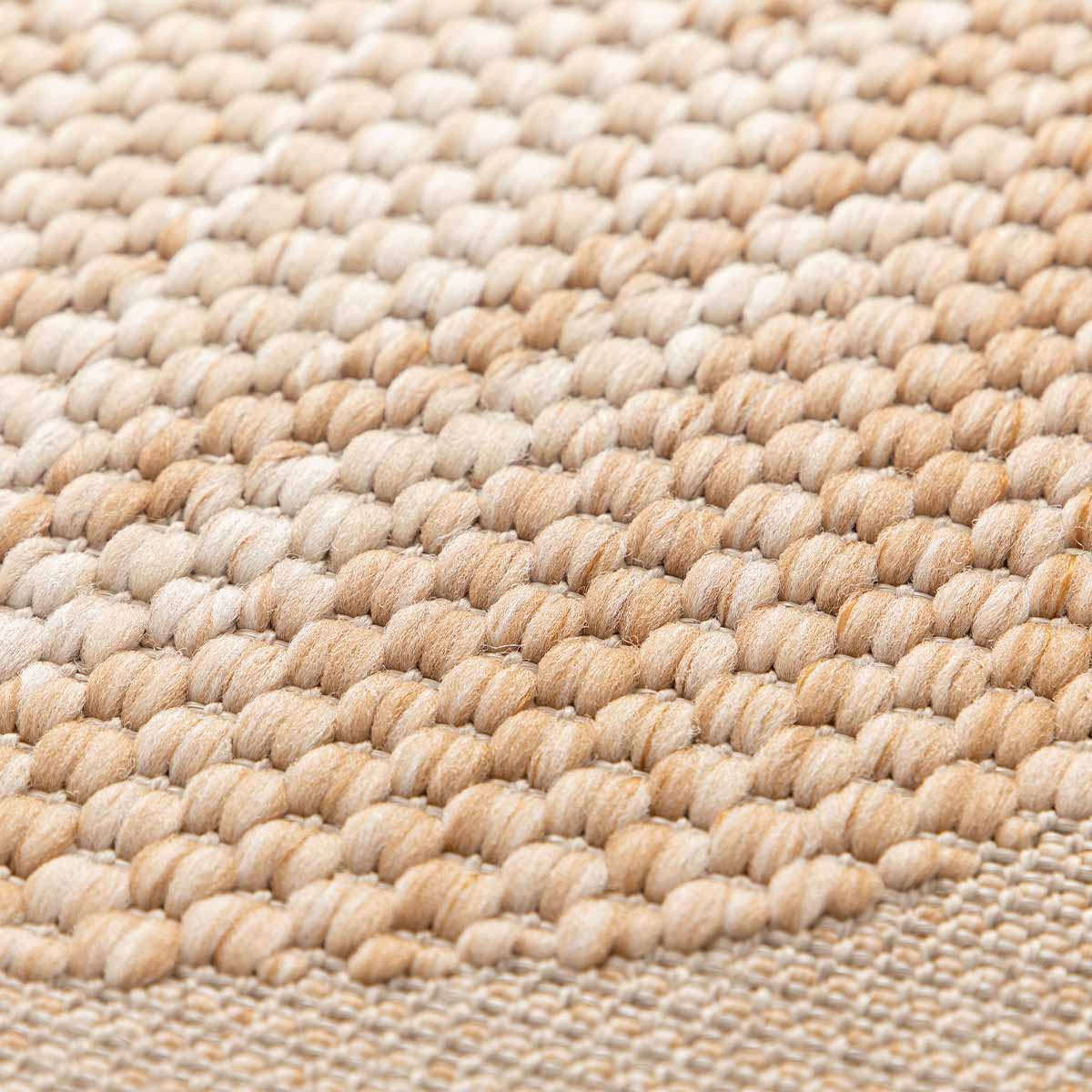 Close-up van een beige tapijt met een textuurpatroon van garenlussen en geweven draden.