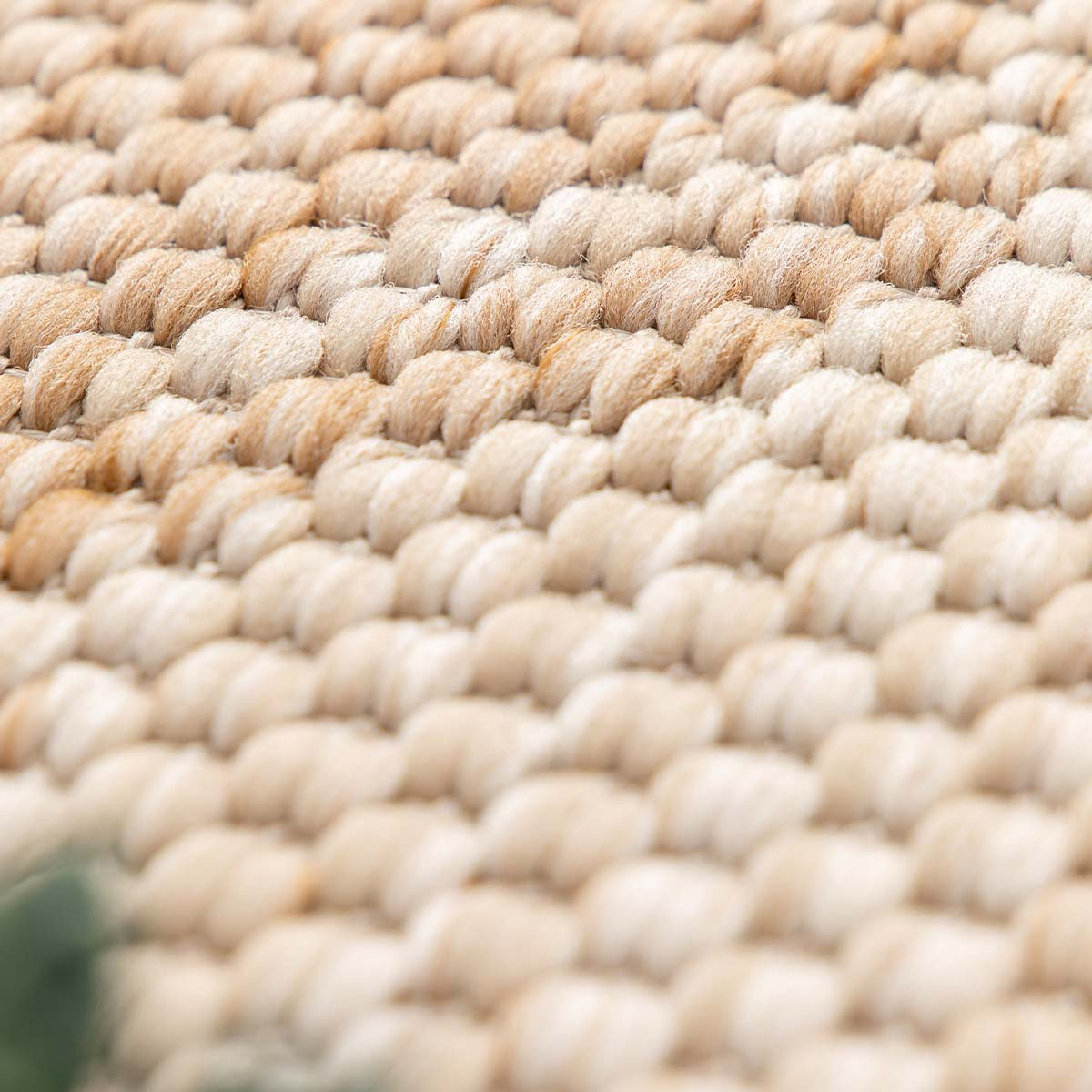 Close-up van beige geweven stof met zichtbare vezels en een groene vlek.