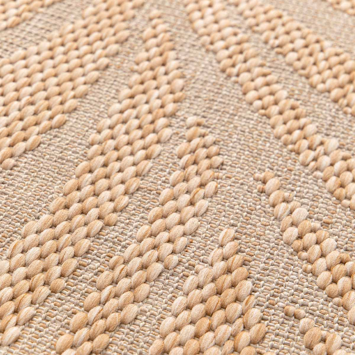 Close-up van een beige vloerkleed met een zigzagpatroon van garenlussen.
