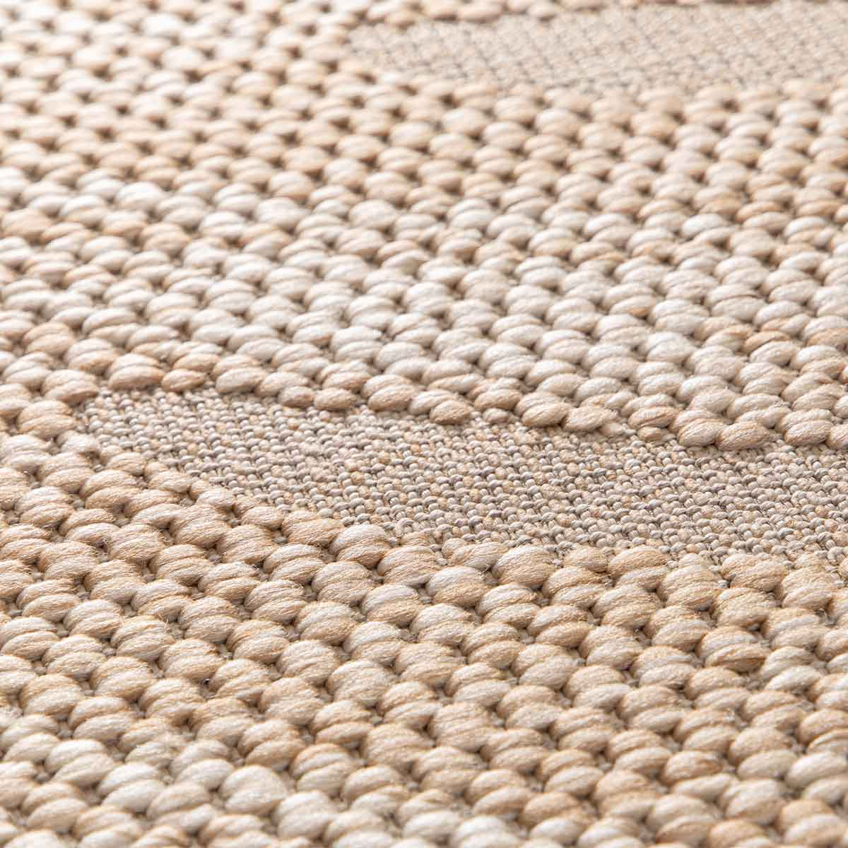 Close-up van een beige vloerkleed met grove textuur en streepjespatroon.