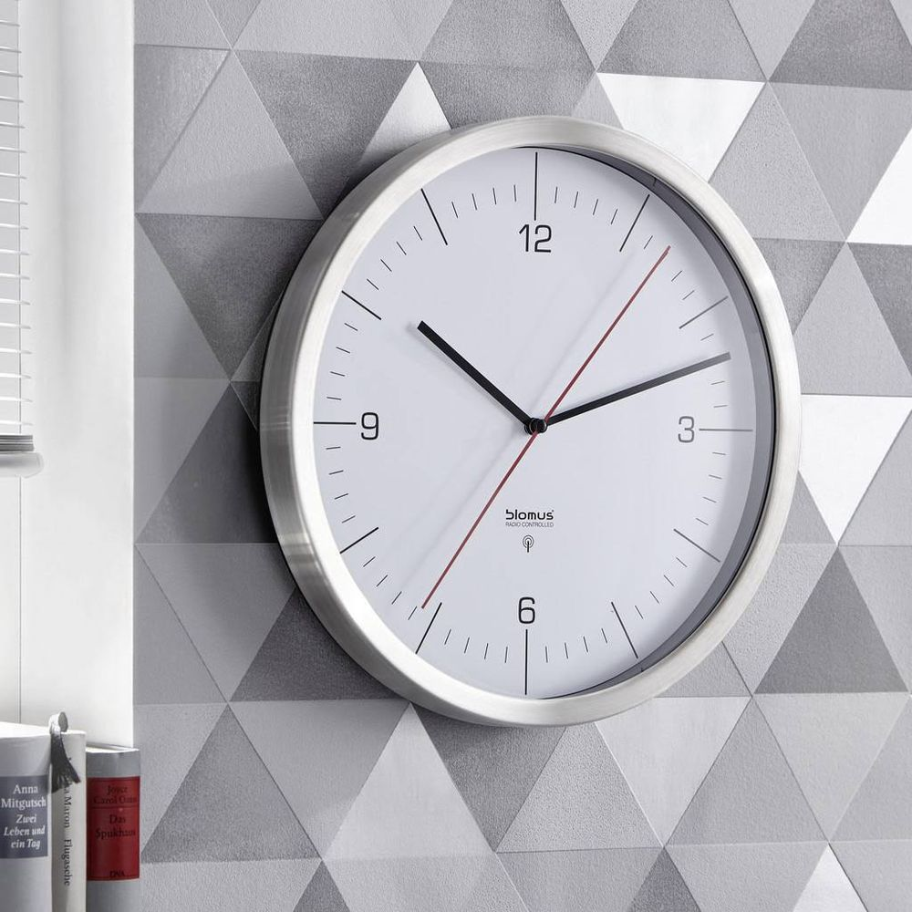 Une horloge murale ronde avec un cadre argenté est accrochée à un mur gris.