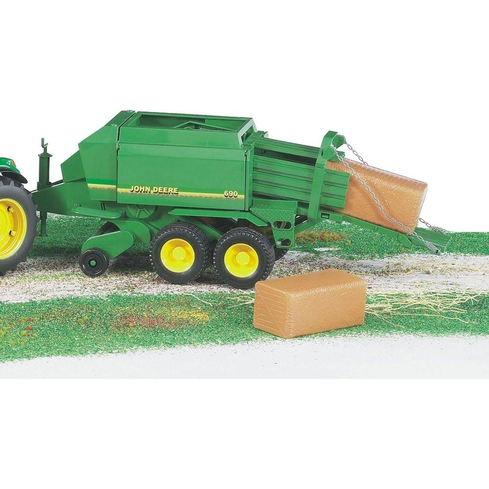 Zielony przyczepa John Deere z jedną belą w wyrzucie i jedną obok.