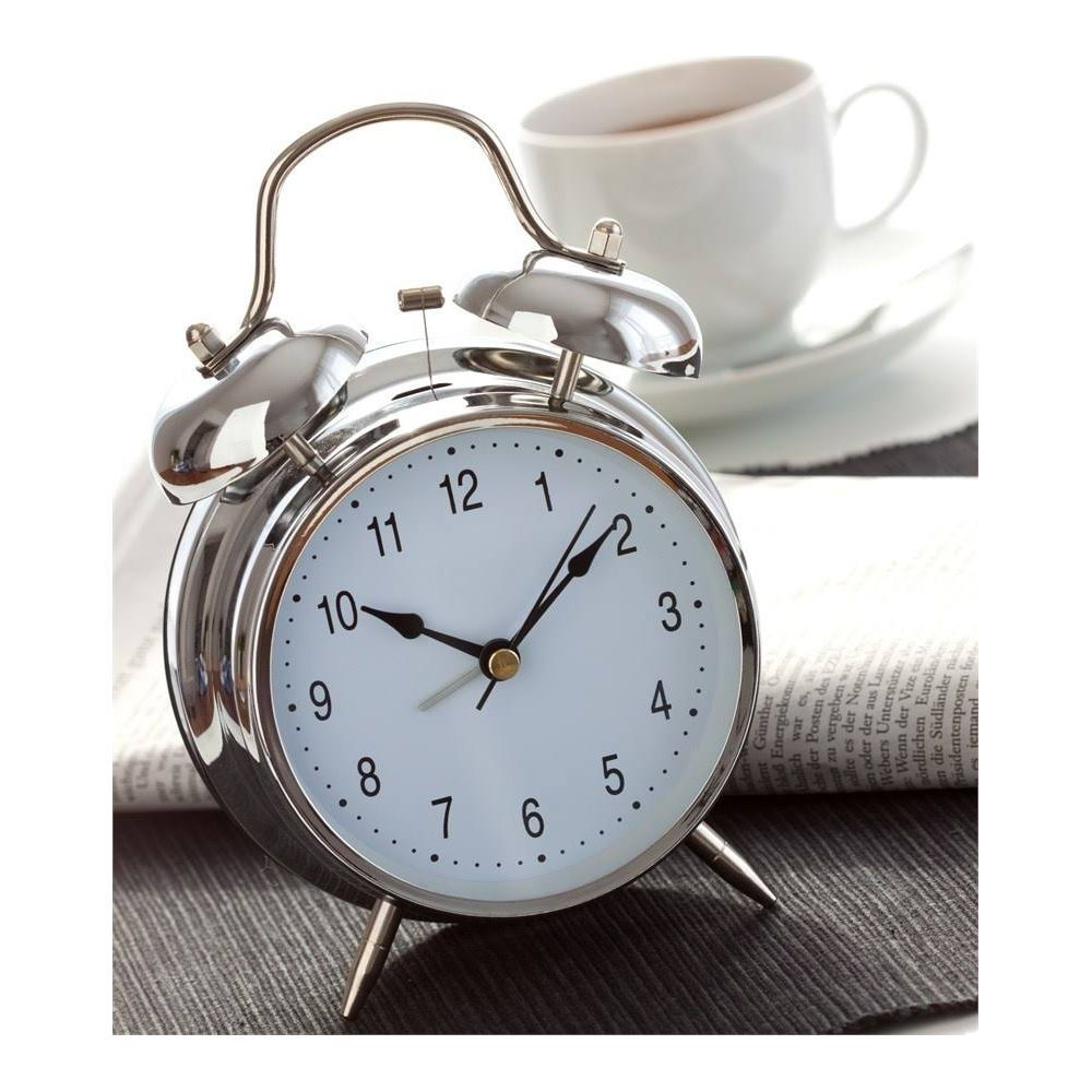 Błyszczący budzik stoi na gazecie, obok filiżanki herbaty.